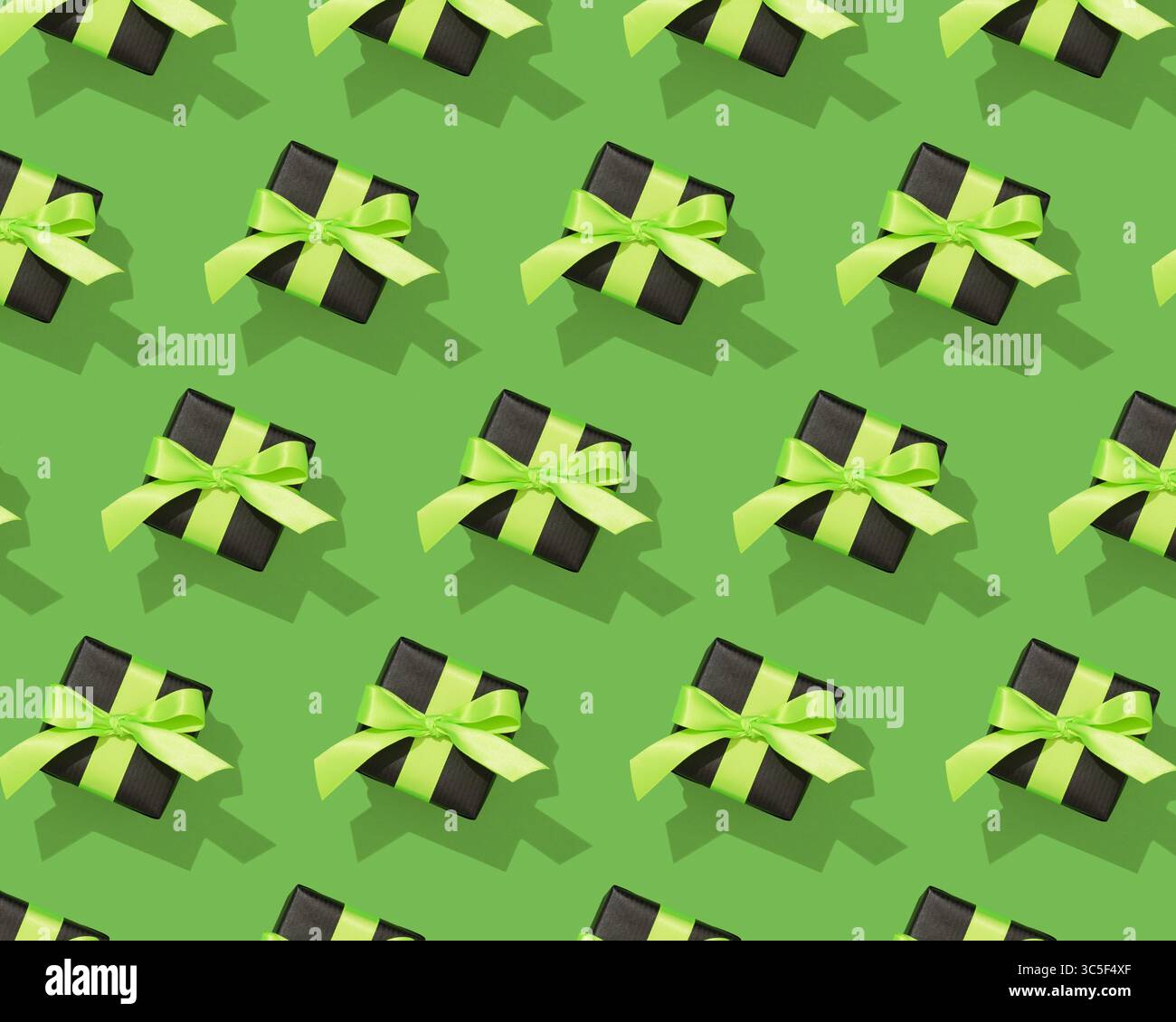 Eleganti confezioni regalo nere con nastri verdi luminosi su uno sfondo verde brillante. Motivo senza cuciture. Foto Stock