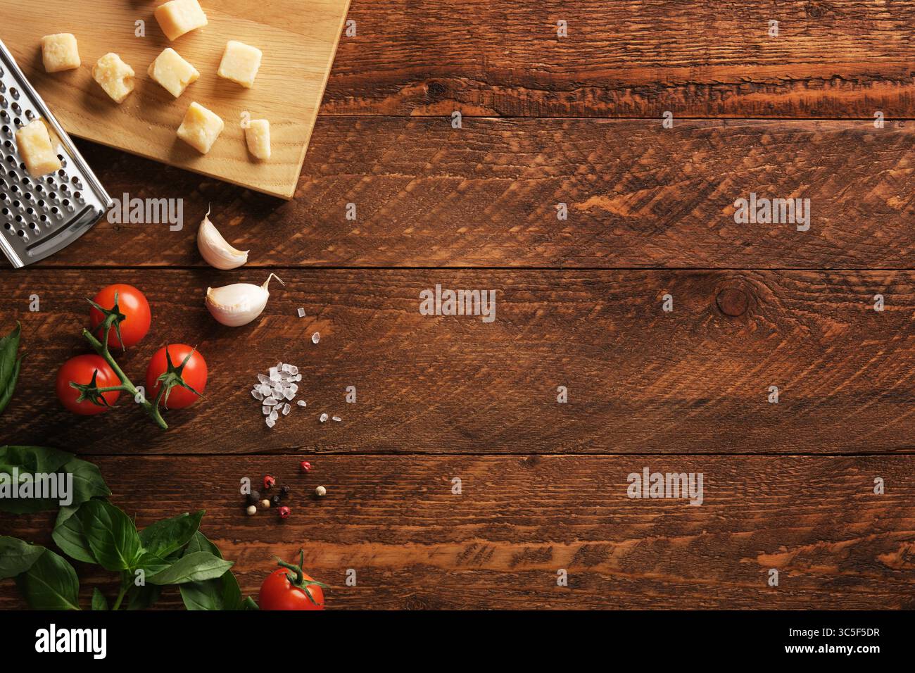 Background culinario. Ingredienti italiani su uno sfondo rustico in legno, pomodori freschi, basilico, aglio e parmigiano. Spazio per il testo. Foto Stock
