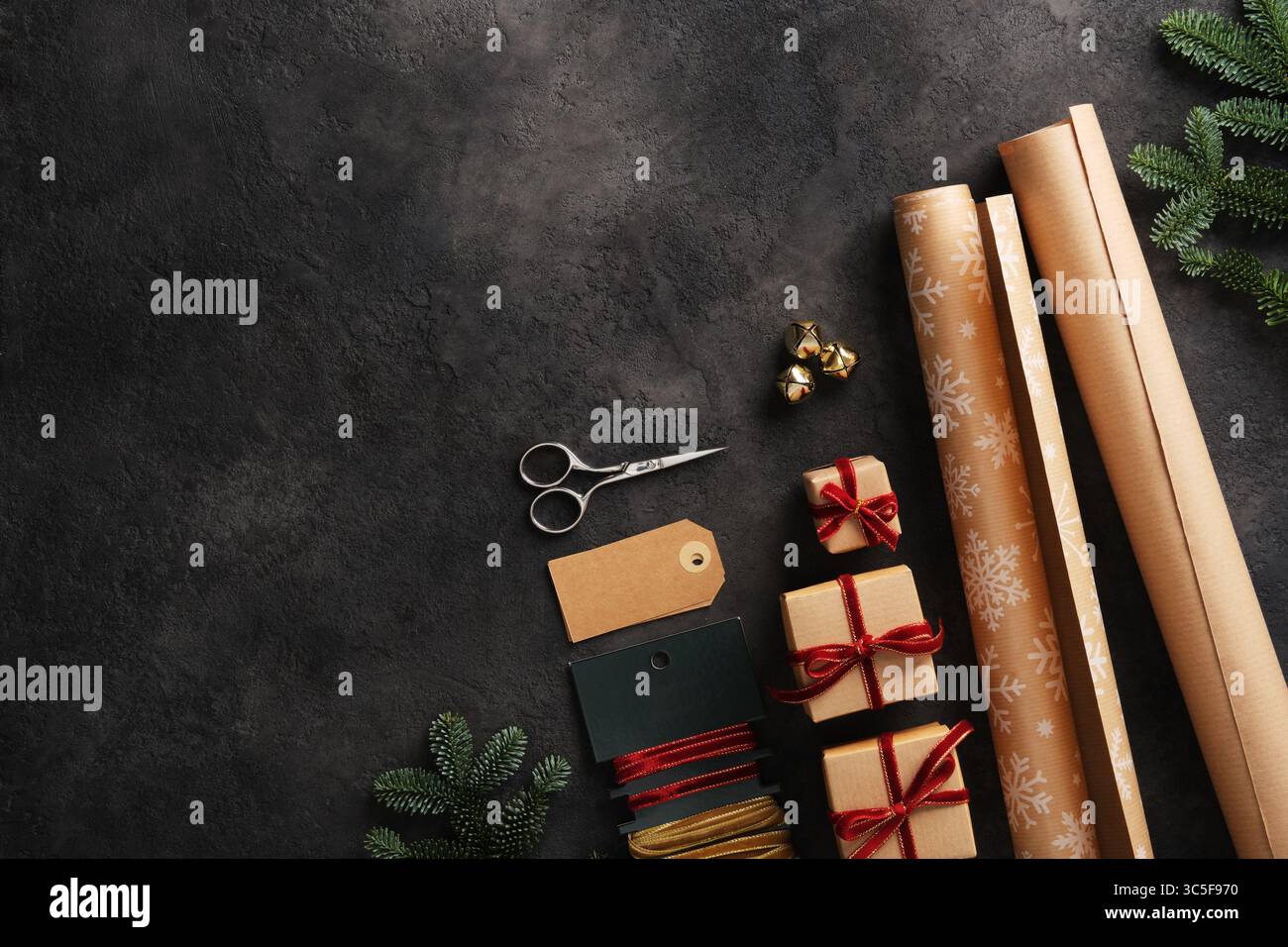 Articoli da imballaggio regalo, rotoli di carta kraft, nastri di velluto, forbici ed etichette su sfondo scuro. Spazio per il testo. Foto Stock