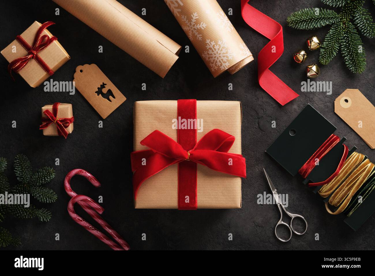 Preparazione per le vacanze, regalo confezionato in una scatola marrone kraft con nastro in velluto rosso e articoli per l'imballaggio regalo ovunque Foto Stock