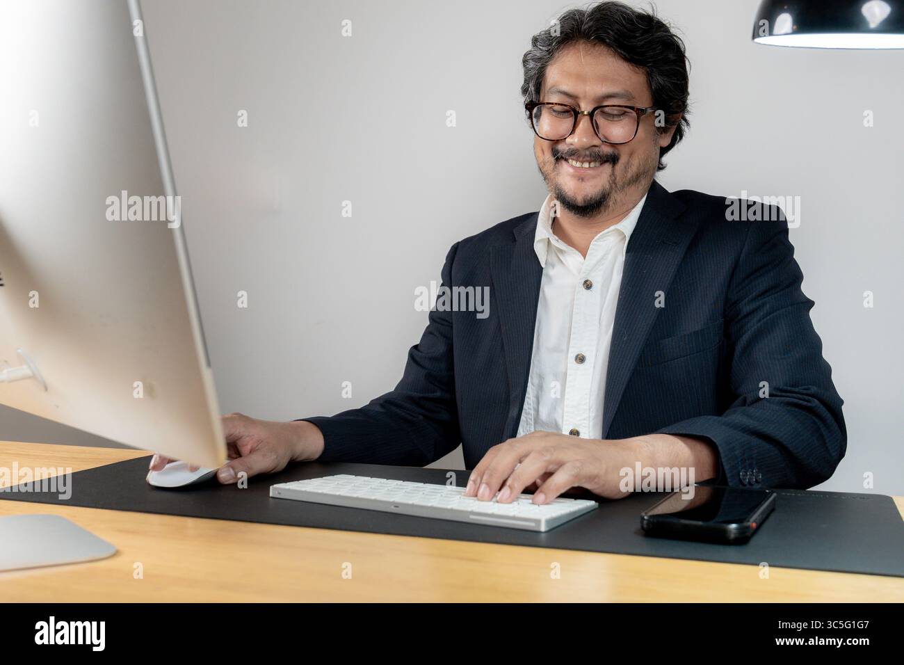 Un allegro dipendente d'ufficio che lavora alla sua scrivania in un ambiente d'ufficio moderno, rappresentando produttività e soddisfazione sul lavoro. Foto Stock