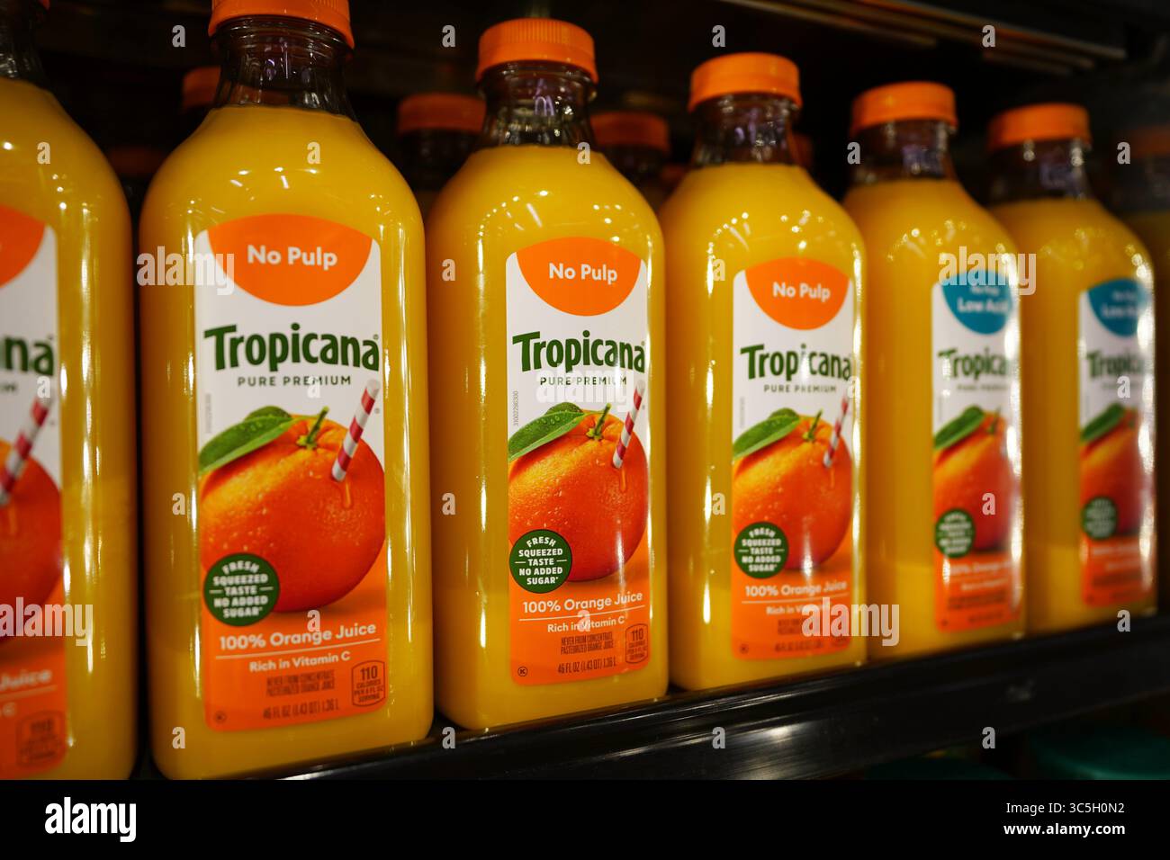 Nuove bottiglie Tropicana Orange Juice esposte in modo vibrante sul ripiano refrigerato del negozio di alimentari Foto Stock