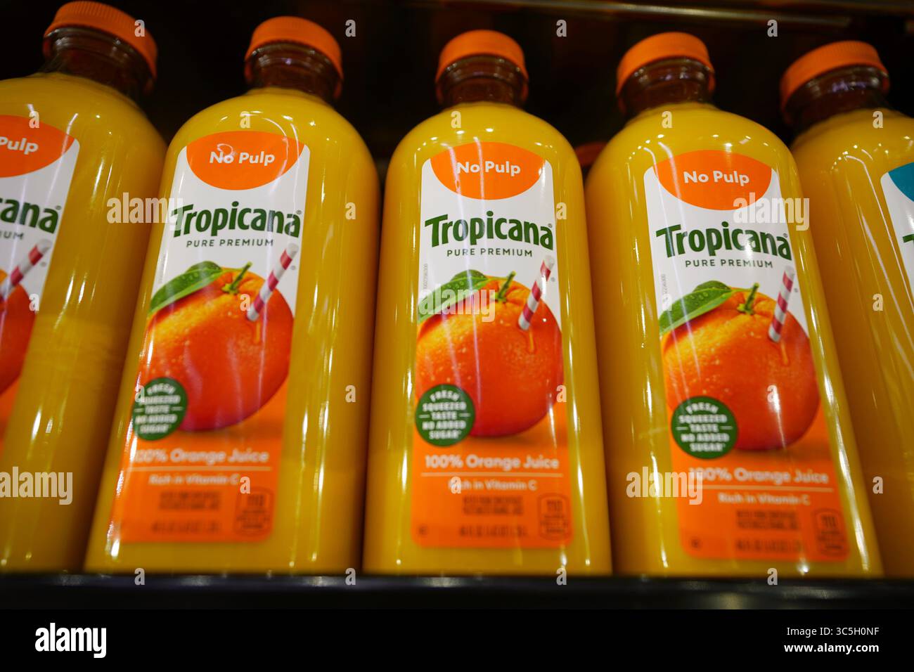 Nuove bottiglie Tropicana Orange Juice esposte in modo vibrante sul ripiano refrigerato del negozio di alimentari Foto Stock