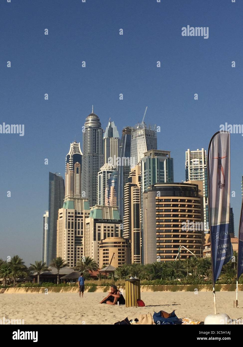 Una splendida vista dell'iconico skyline di Dubai che si erge dietro una spiaggia soleggiata, dove l'architettura futuristica incontra la serenità della costa del Golfo Persico. Foto Stock