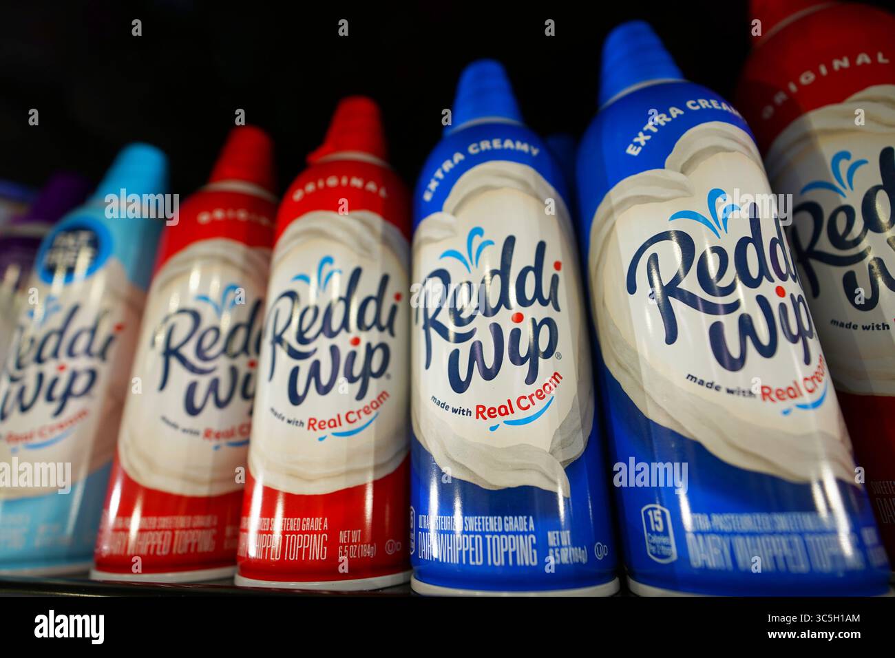 Lattine di panna montata Reddi WIP perfettamente allineate sul ripiano della drogheria con ugello visibile Foto Stock