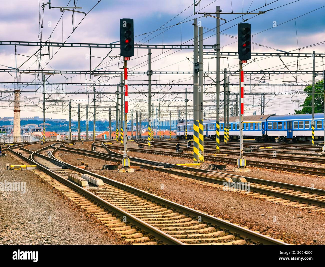 Binari ferroviari e linee elettriche aeree alla stazione ferroviaria - background industriale astratto con segnali rossi e treno passeggeri blu, ideale per sfondo, Web Design, pubblicità e uso digitale Foto Stock