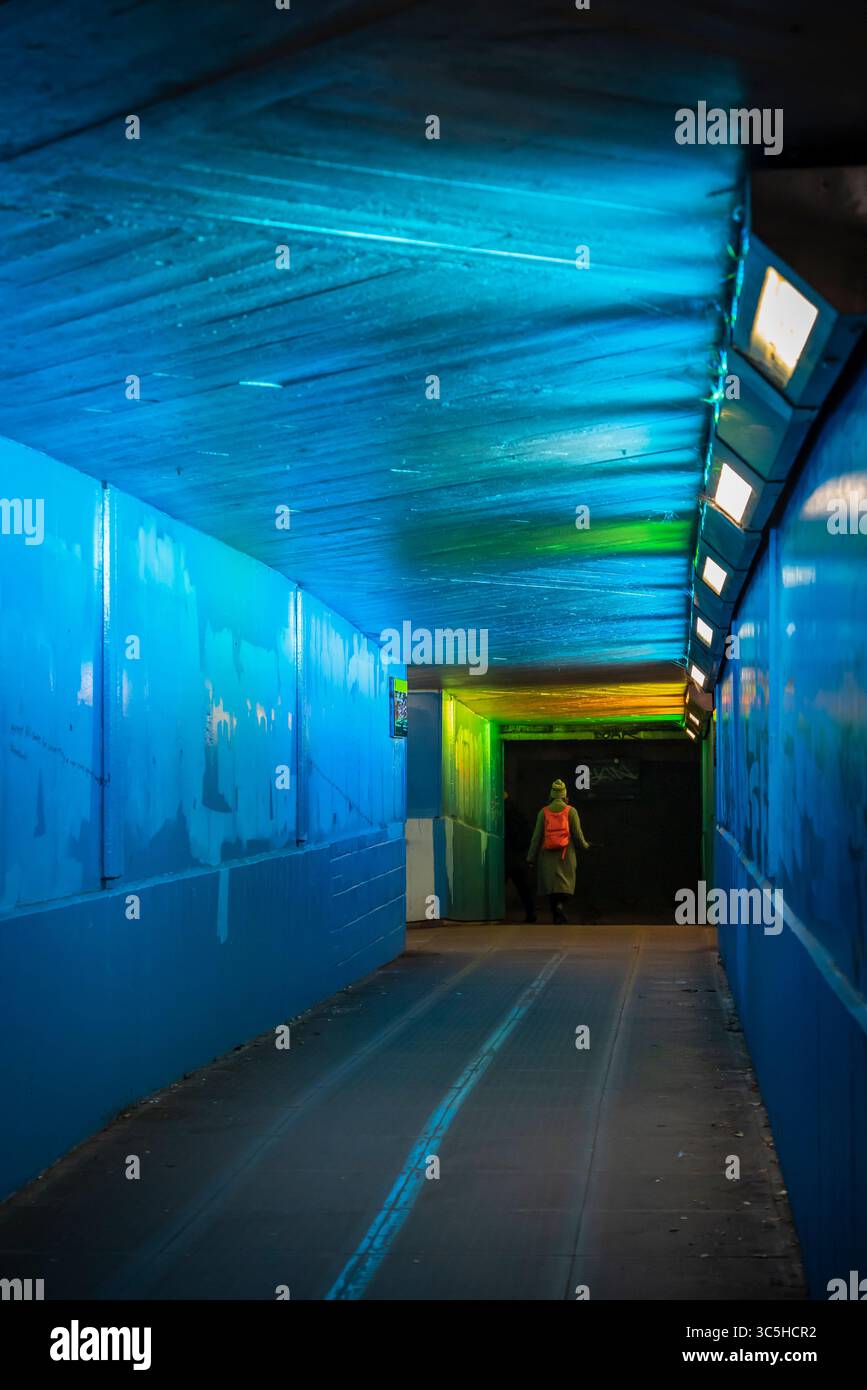 Donna con uno zaino rosso che cammina in inverno attraverso un sottopassaggio urbano illuminato da sola, Londra, Inghilterra, Regno Unito Foto Stock