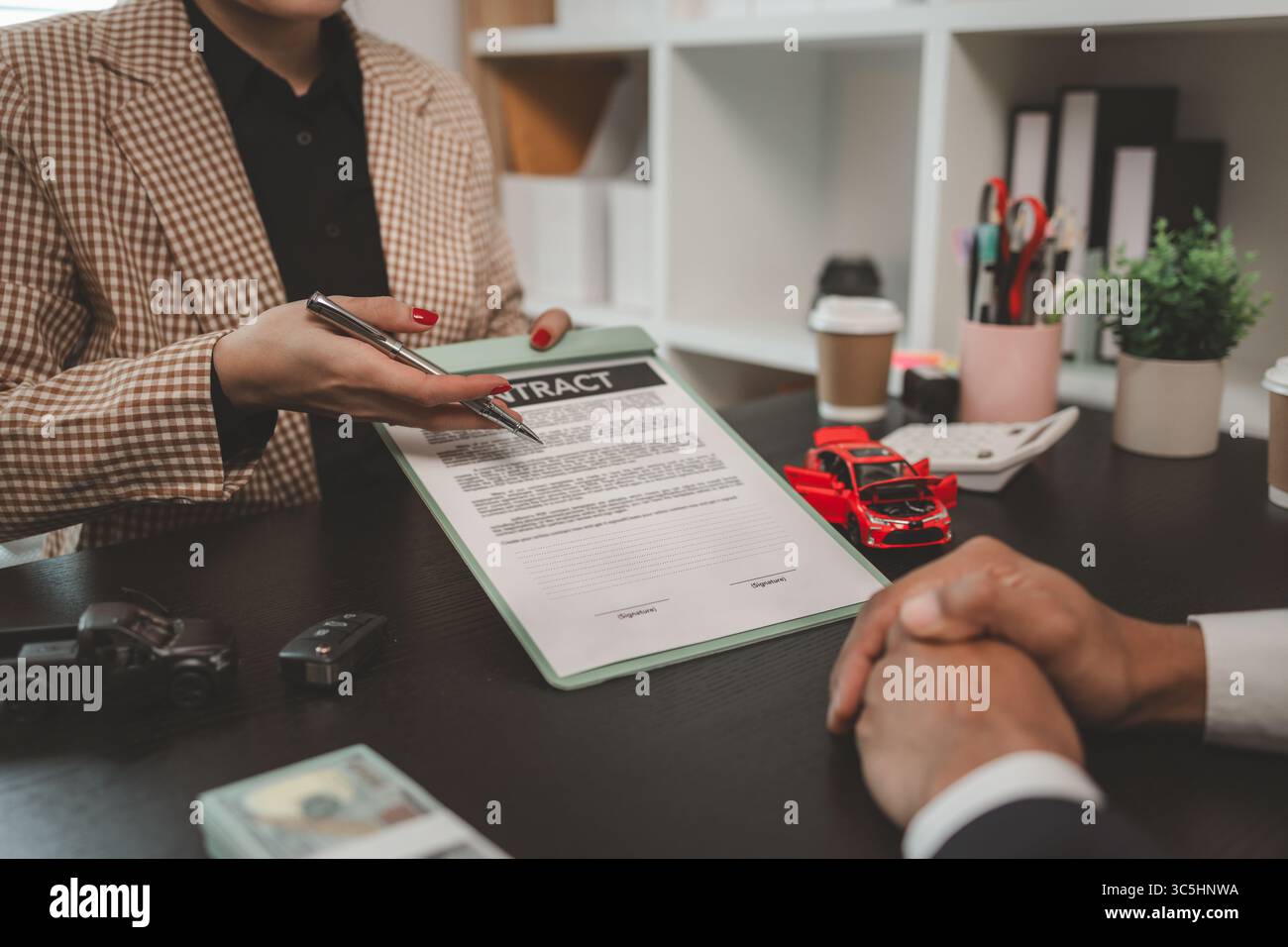 un venditore di auto sta spiegando i dettagli di un contratto di acquisto di un'auto all'acquirente prima di firmare il contratto di vendita, lo showroom, il concessionario, il contratto auto, Foto Stock