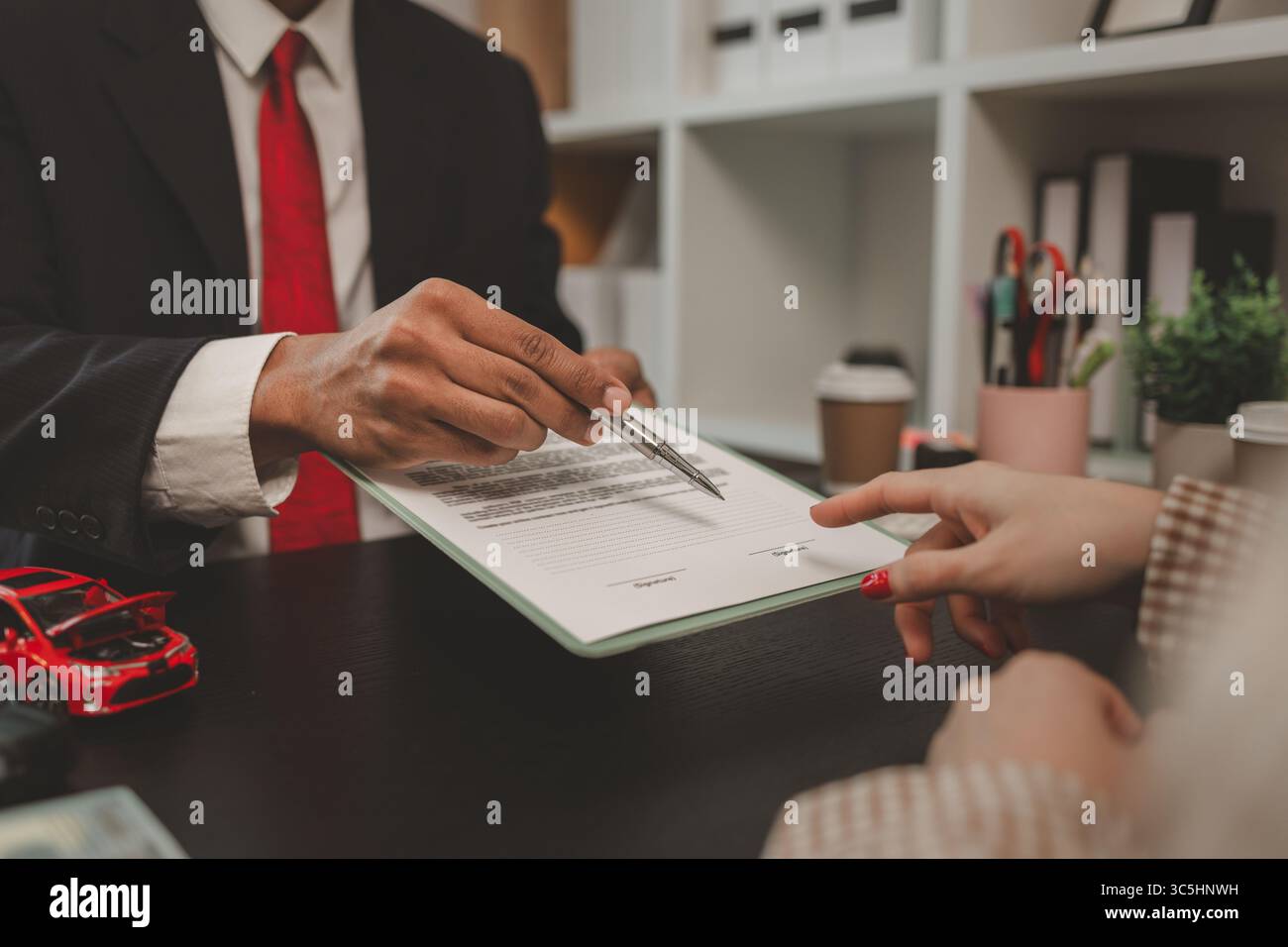 un venditore di auto sta spiegando i dettagli di un contratto di acquisto di un'auto all'acquirente prima di firmare il contratto di vendita, lo showroom, il concessionario, il contratto auto, Foto Stock