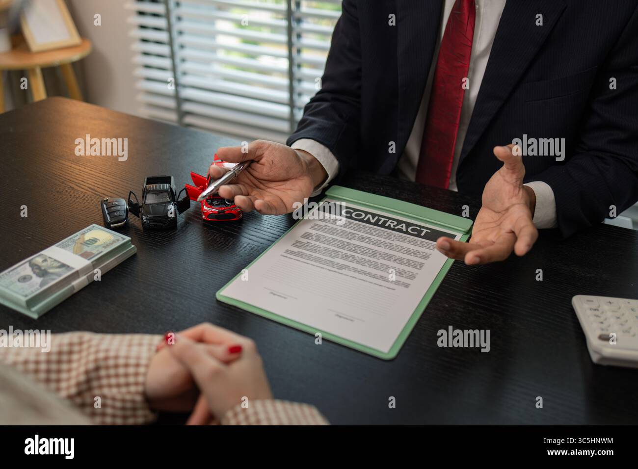un venditore di auto sta spiegando i dettagli di un contratto di acquisto di un'auto all'acquirente prima di firmare il contratto di vendita, lo showroom, il concessionario, il contratto auto, Foto Stock