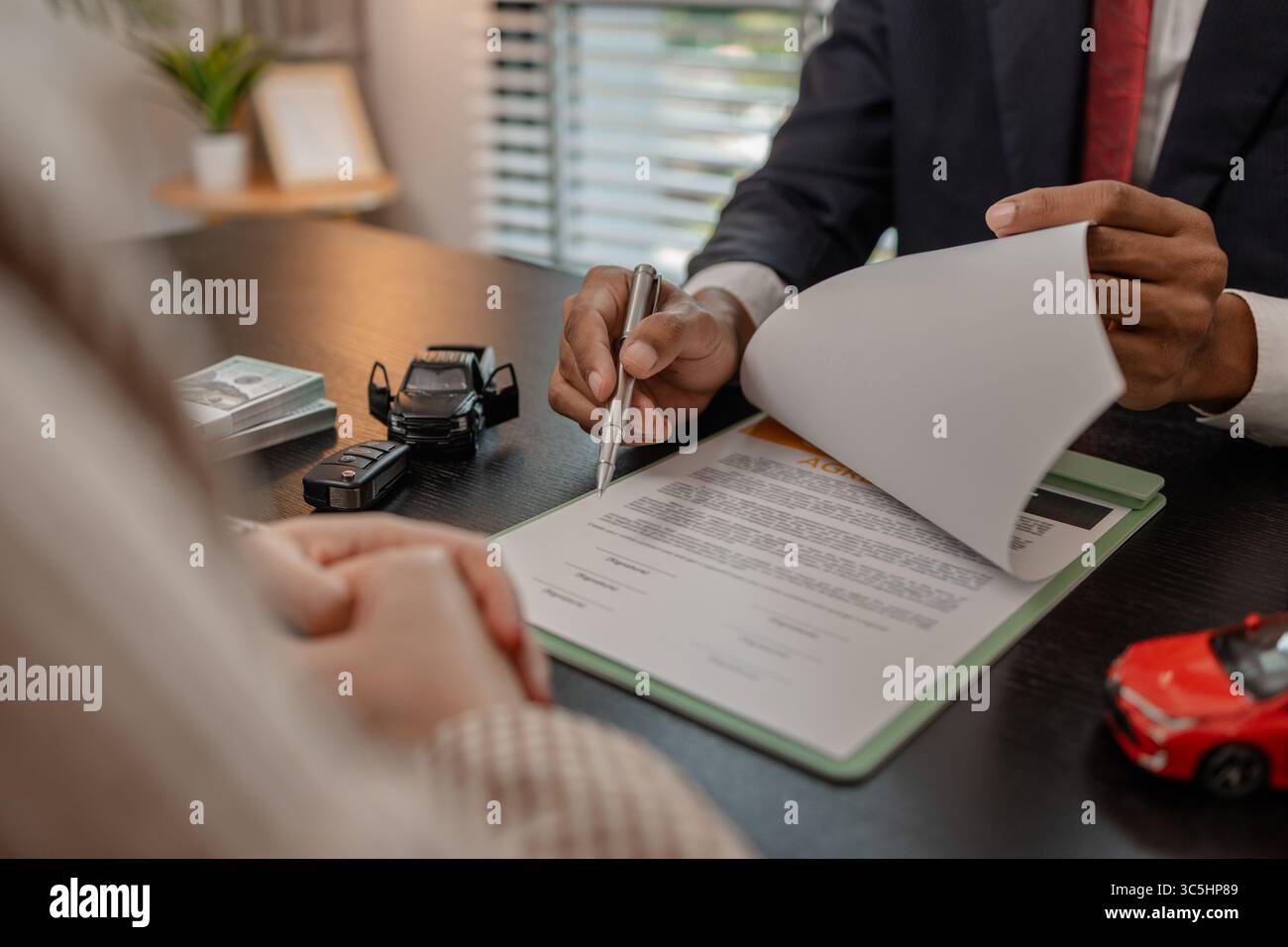 un venditore di auto sta spiegando i dettagli di un contratto di acquisto di un'auto all'acquirente prima di firmare il contratto di vendita, lo showroom, il concessionario, il contratto auto, Foto Stock