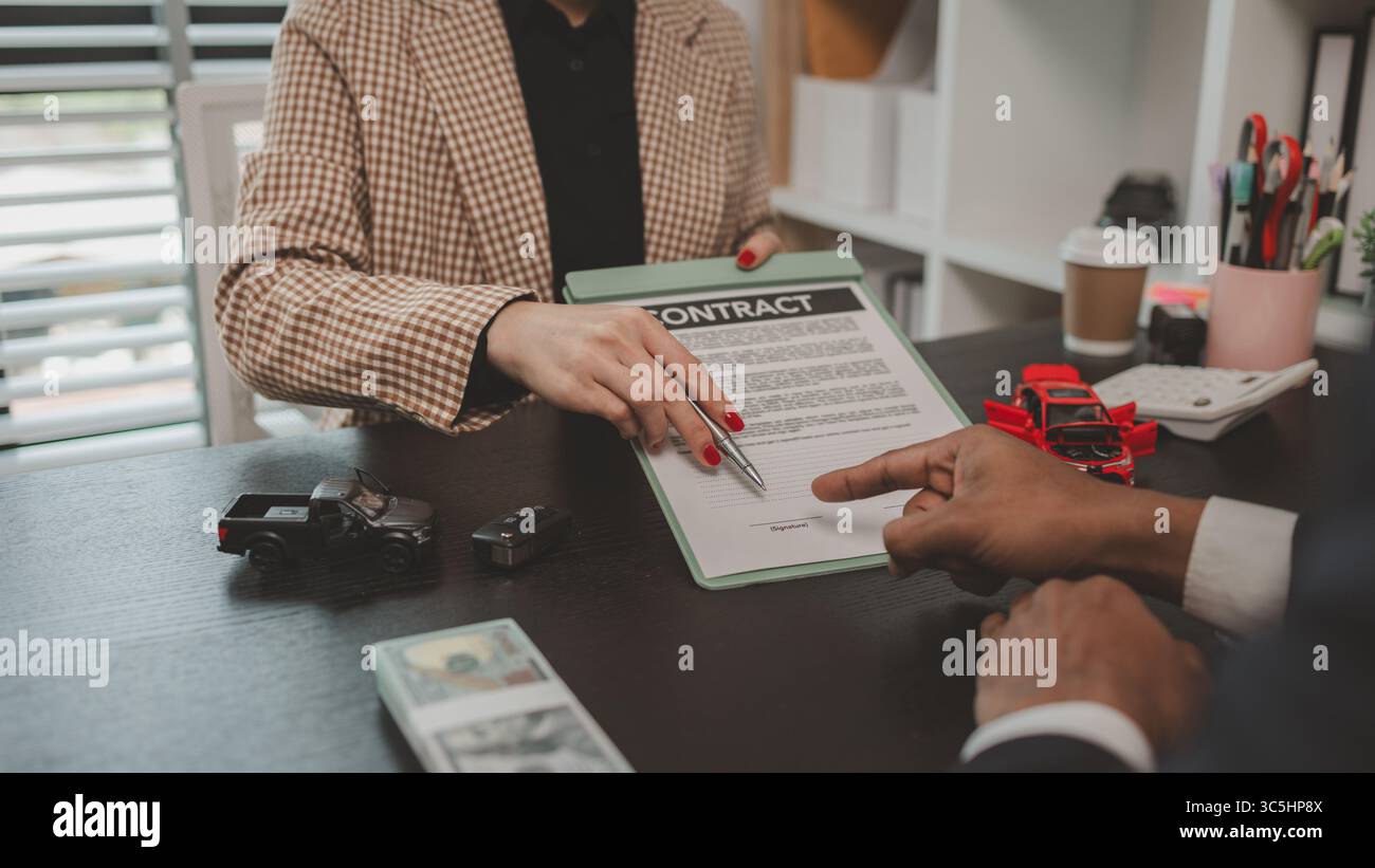 un venditore di auto sta spiegando i dettagli di un contratto di acquisto di un'auto all'acquirente prima di firmare il contratto di vendita, lo showroom, il concessionario, il contratto auto, Foto Stock