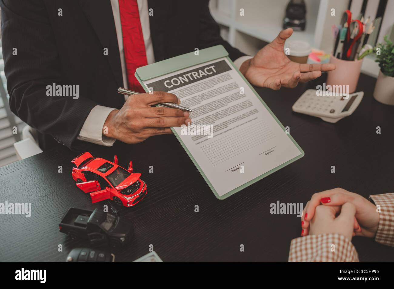 un venditore di auto sta spiegando i dettagli di un contratto di acquisto di un'auto all'acquirente prima di firmare il contratto di vendita, lo showroom, il concessionario, il contratto auto, Foto Stock