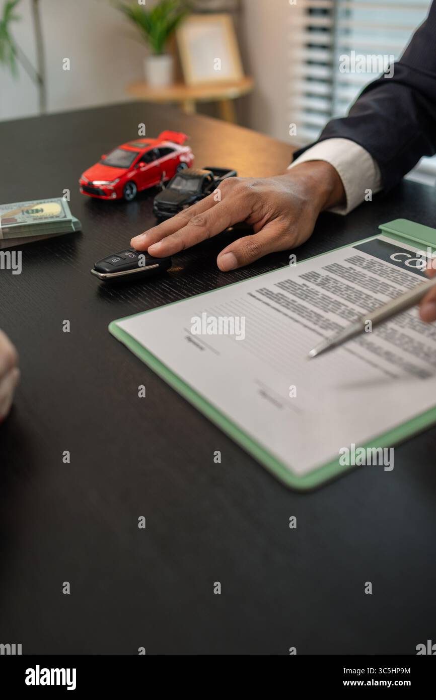 un venditore di auto sta spiegando i dettagli di un contratto di acquisto di un'auto all'acquirente prima di firmare il contratto di vendita, lo showroom, il concessionario, il contratto auto, Foto Stock