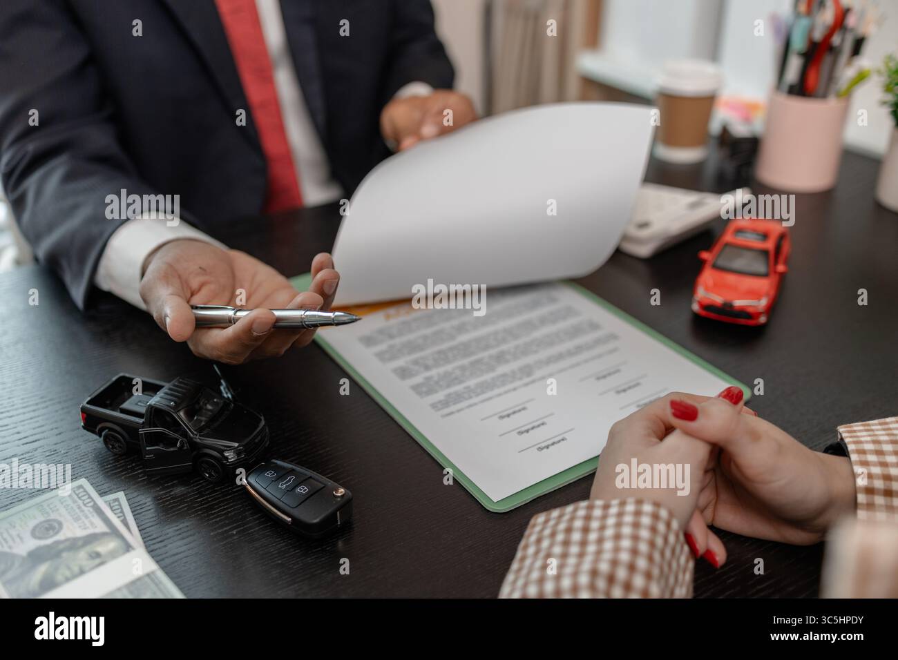 un venditore di auto sta spiegando i dettagli di un contratto di acquisto di un'auto all'acquirente prima di firmare il contratto di vendita, lo showroom, il concessionario, il contratto auto, Foto Stock