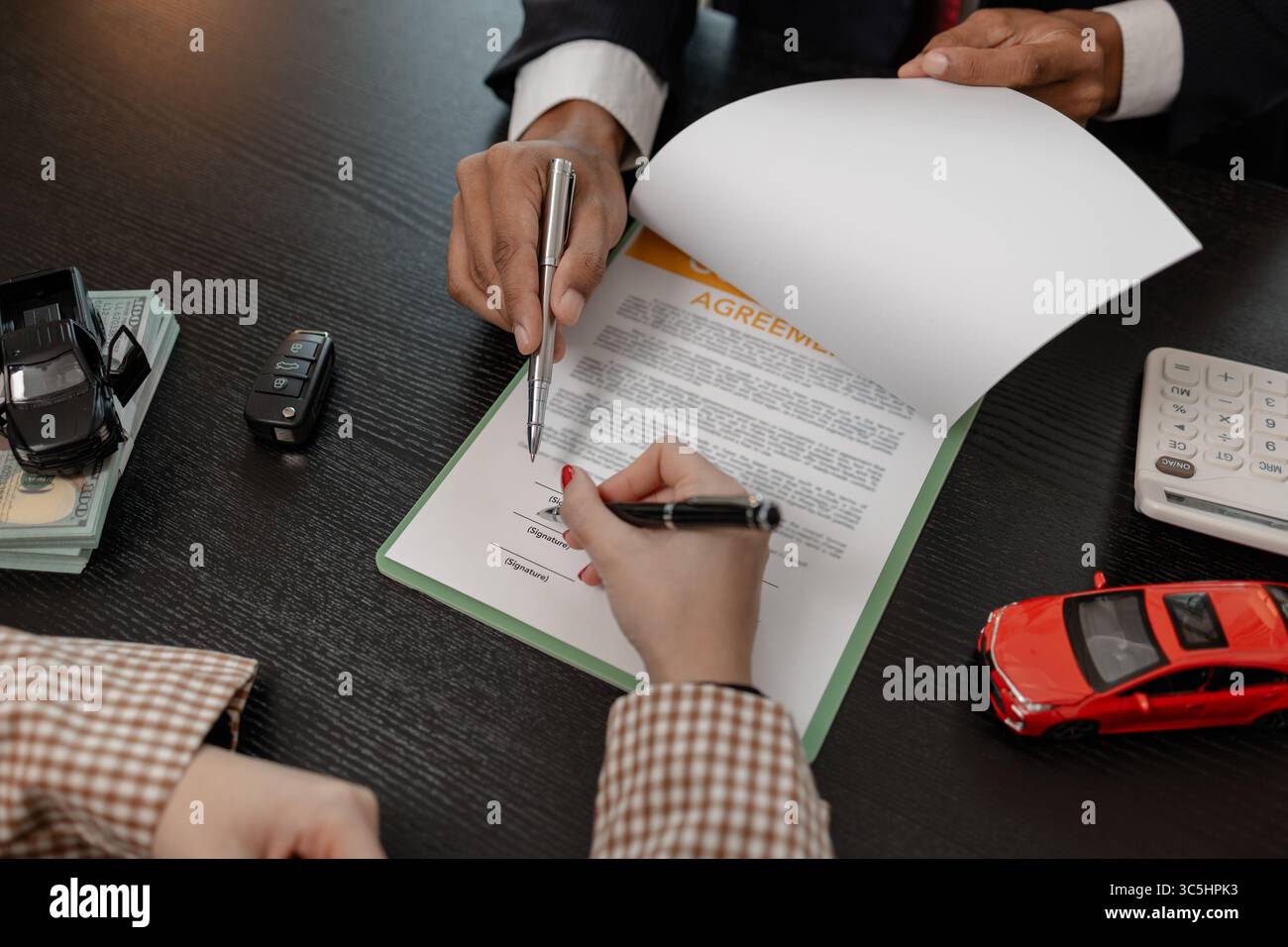 un venditore di auto sta spiegando i dettagli di un contratto di acquisto di un'auto all'acquirente prima di firmare il contratto di vendita, lo showroom, il concessionario, il contratto auto, Foto Stock