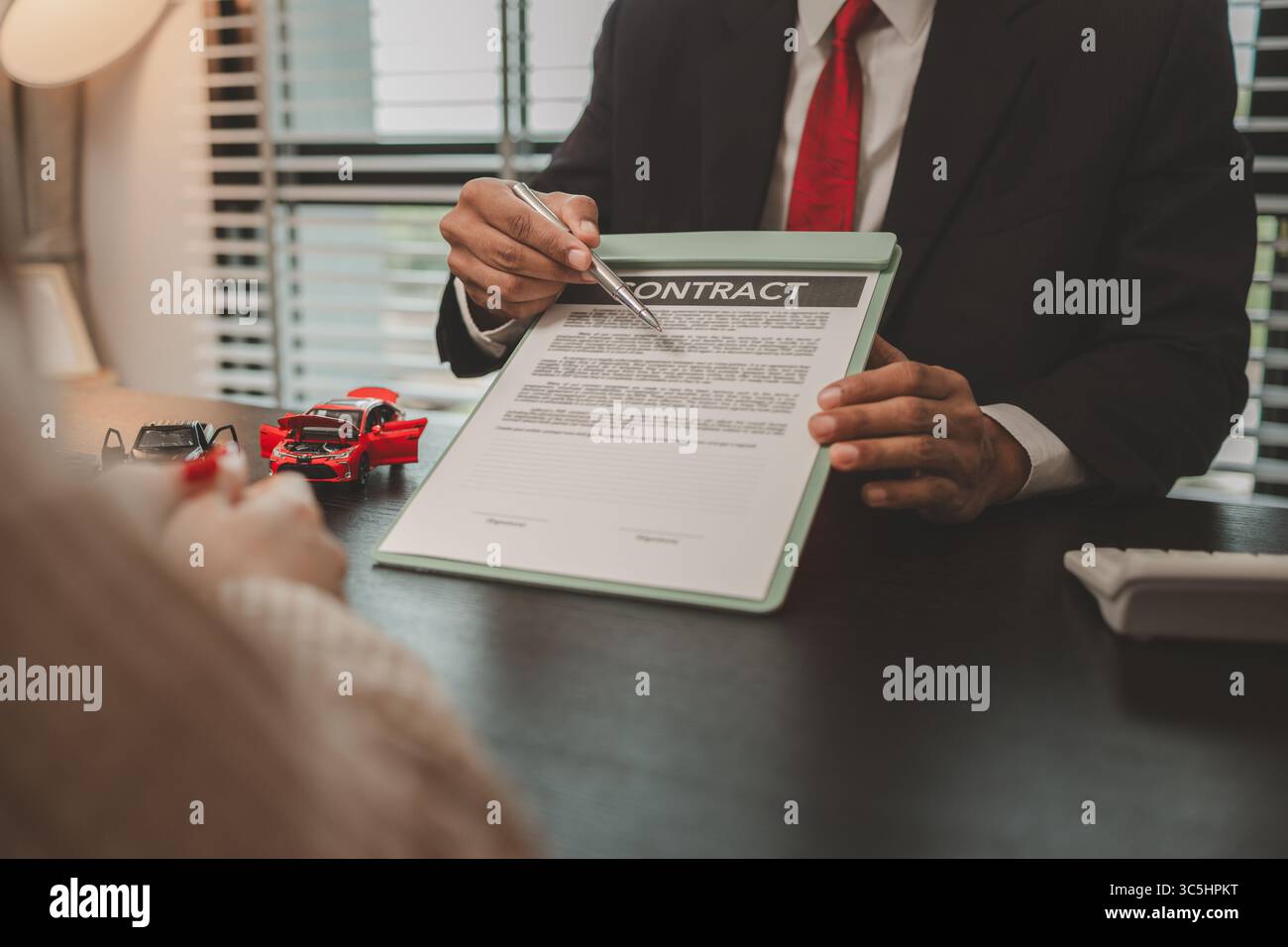 un venditore di auto sta spiegando i dettagli di un contratto di acquisto di un'auto all'acquirente prima di firmare il contratto di vendita, lo showroom, il concessionario, il contratto auto, Foto Stock