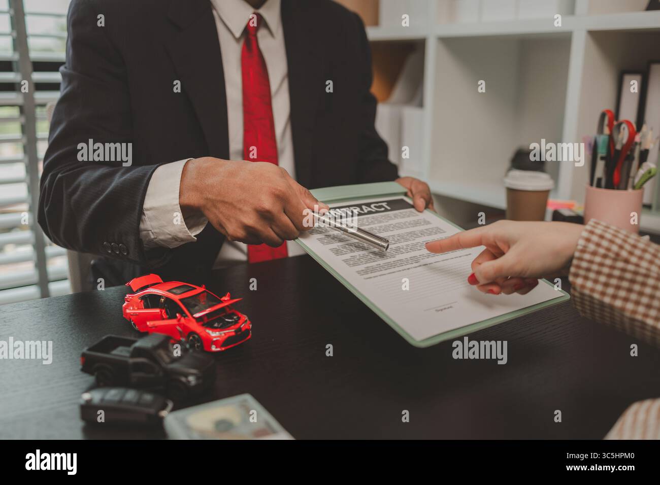 un venditore di auto sta spiegando i dettagli di un contratto di acquisto di un'auto all'acquirente prima di firmare il contratto di vendita, lo showroom, il concessionario, il contratto auto, Foto Stock