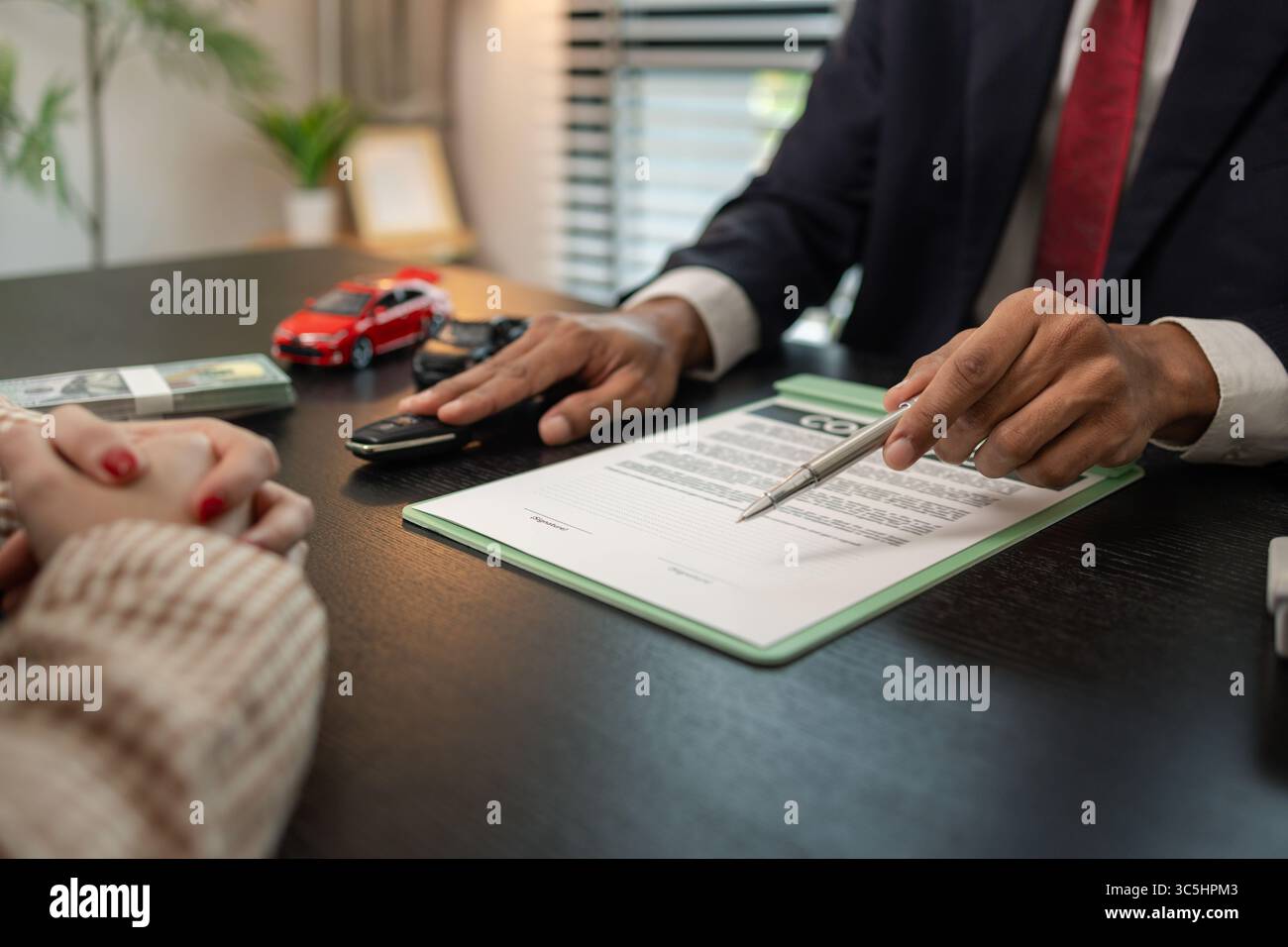 un venditore di auto sta spiegando i dettagli di un contratto di acquisto di un'auto all'acquirente prima di firmare il contratto di vendita, lo showroom, il concessionario, il contratto auto, Foto Stock