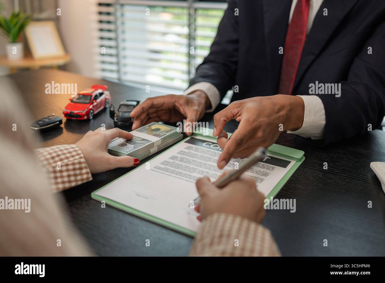 un venditore di auto sta spiegando i dettagli di un contratto di acquisto di un'auto all'acquirente prima di firmare il contratto di vendita, lo showroom, il concessionario, il contratto auto, Foto Stock
