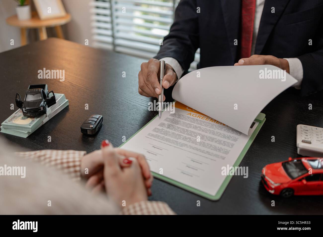 un venditore di auto sta spiegando i dettagli di un contratto di acquisto di un'auto all'acquirente prima di firmare il contratto di vendita, lo showroom, il concessionario, il contratto auto, Foto Stock