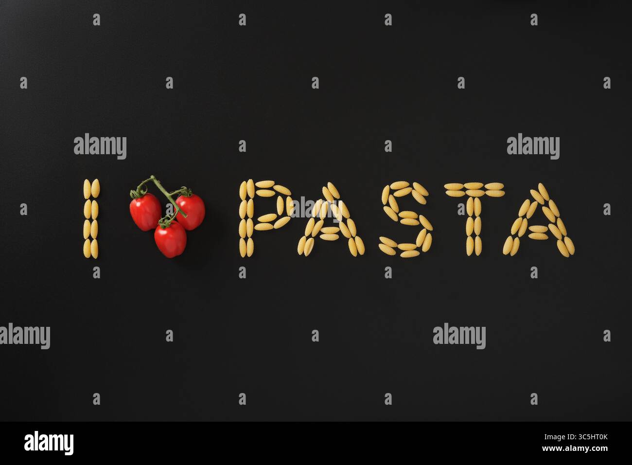 Frase adoro la pasta fatta con pasta secca e pomodori ciliegini a forma di cuore su sfondo nero. Concetto di passione per il cibo e cucina italiana. Foto Stock