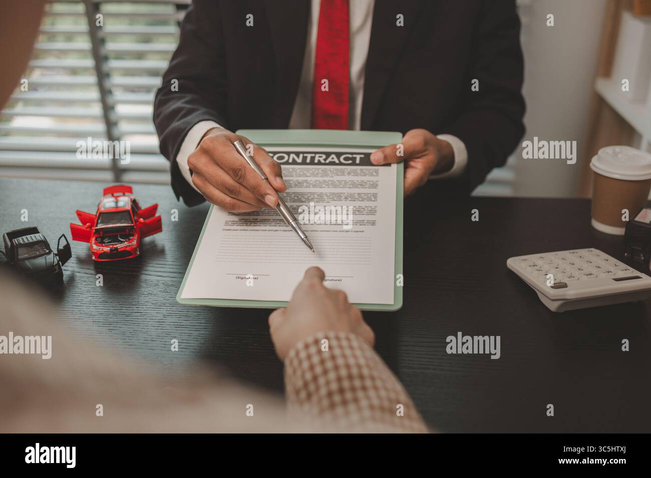 un venditore di auto sta spiegando i dettagli di un contratto di acquisto di un'auto all'acquirente prima di firmare il contratto di vendita, lo showroom, il concessionario, il contratto auto, Foto Stock