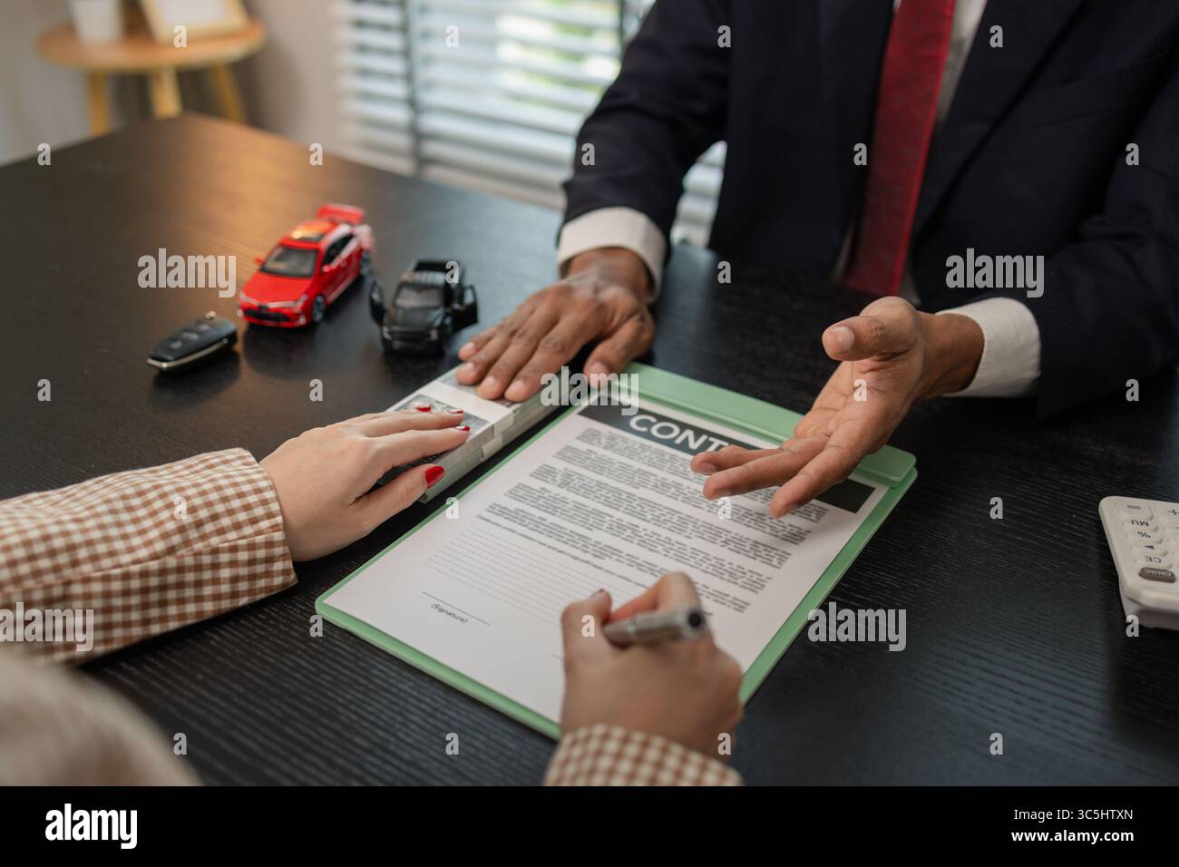 un venditore di auto sta spiegando i dettagli di un contratto di acquisto di un'auto all'acquirente prima di firmare il contratto di vendita, lo showroom, il concessionario, il contratto auto, Foto Stock