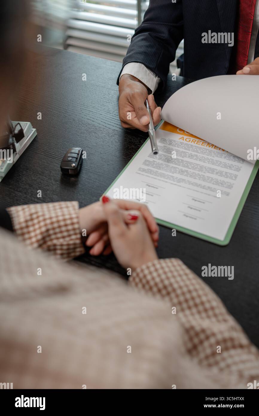 un venditore di auto sta spiegando i dettagli di un contratto di acquisto di un'auto all'acquirente prima di firmare il contratto di vendita, lo showroom, il concessionario, il contratto auto, Foto Stock