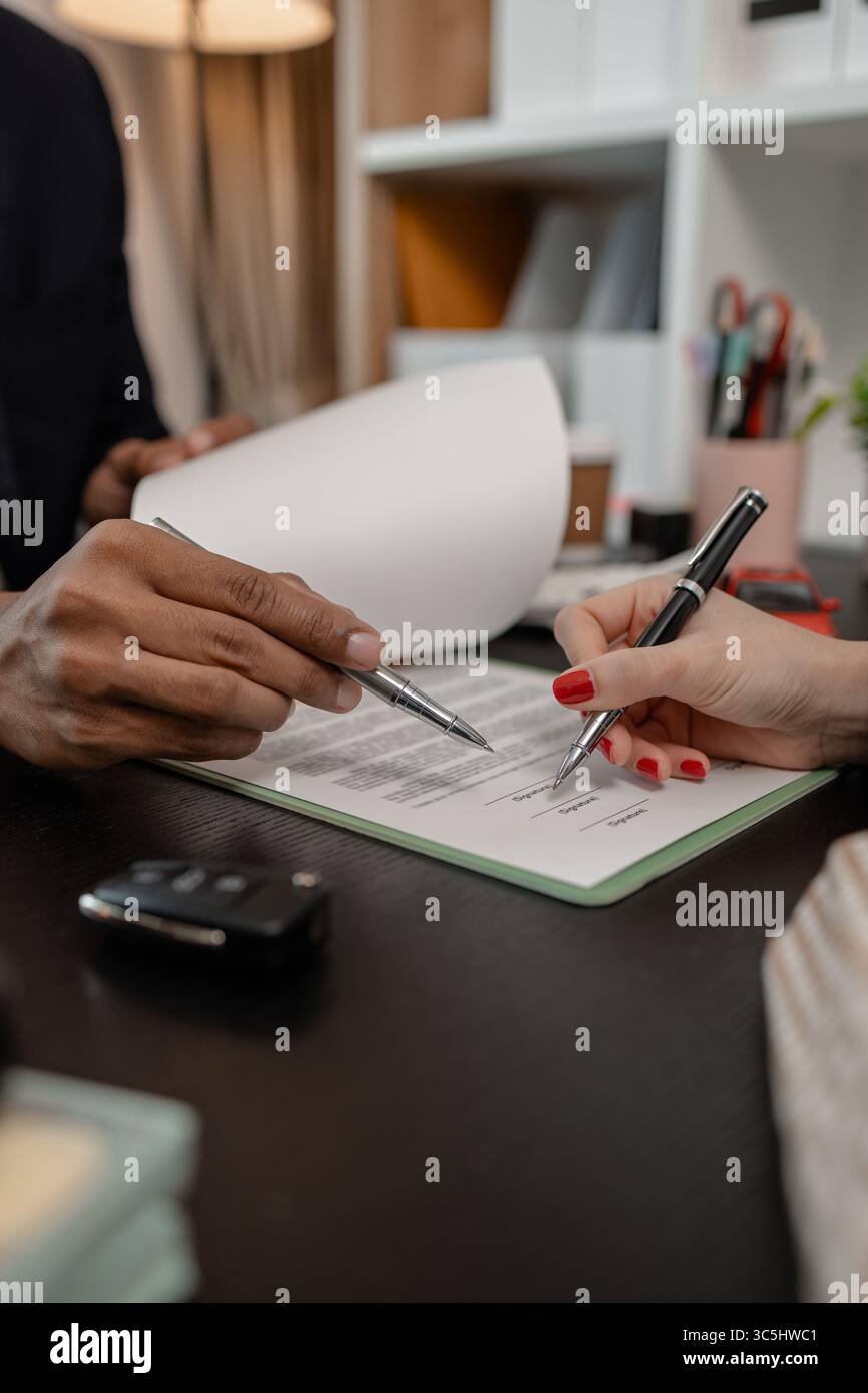 un venditore di auto sta spiegando i dettagli di un contratto di acquisto di un'auto all'acquirente prima di firmare il contratto di vendita, lo showroom, il concessionario, il contratto auto, Foto Stock