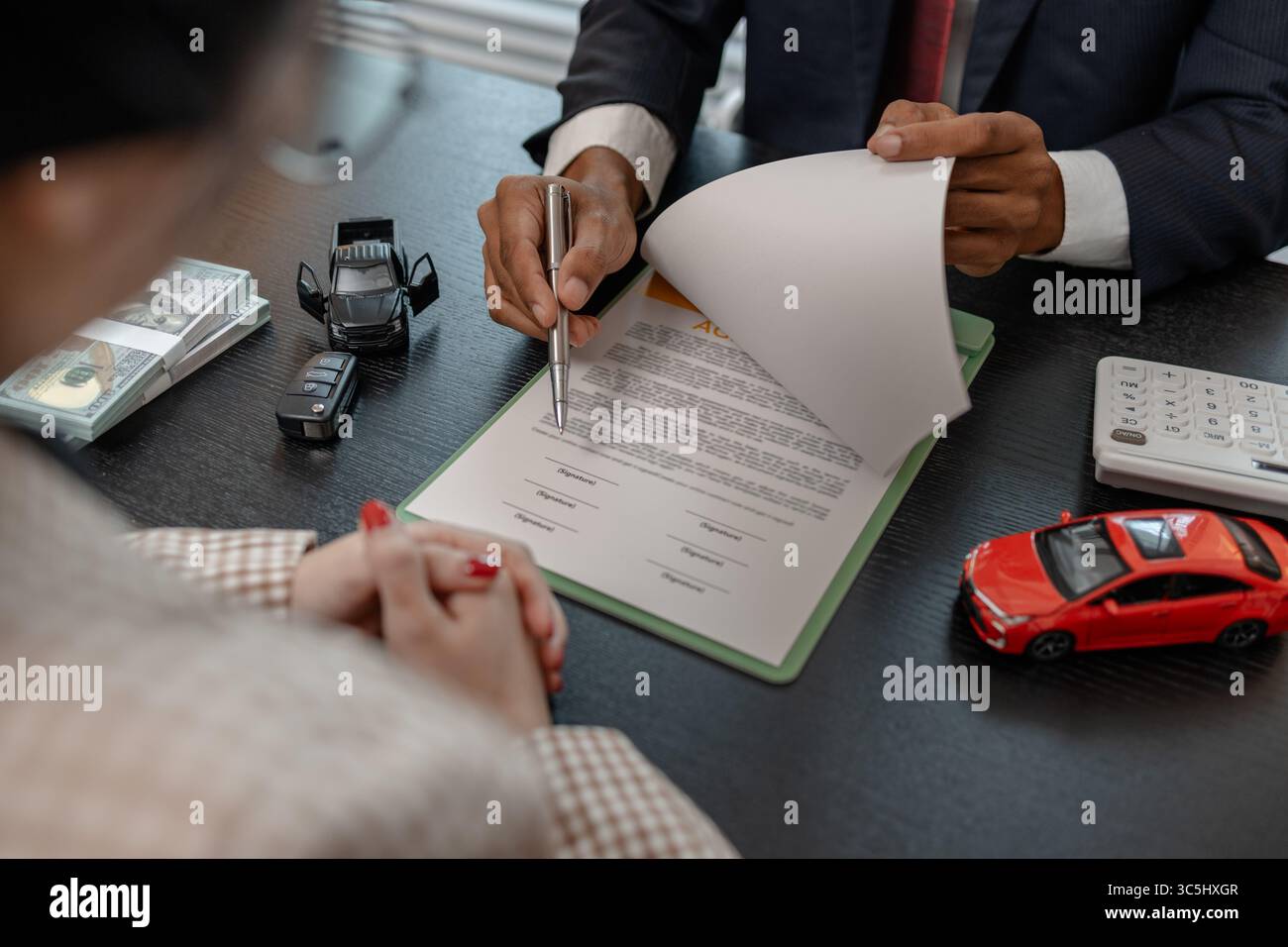 un venditore di auto sta spiegando i dettagli di un contratto di acquisto di un'auto all'acquirente prima di firmare il contratto di vendita, lo showroom, il concessionario, il contratto auto, Foto Stock