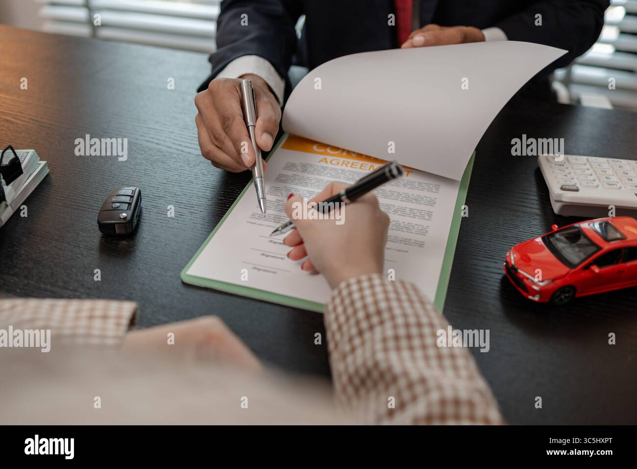 un venditore di auto sta spiegando i dettagli di un contratto di acquisto di un'auto all'acquirente prima di firmare il contratto di vendita, lo showroom, il concessionario, il contratto auto, Foto Stock