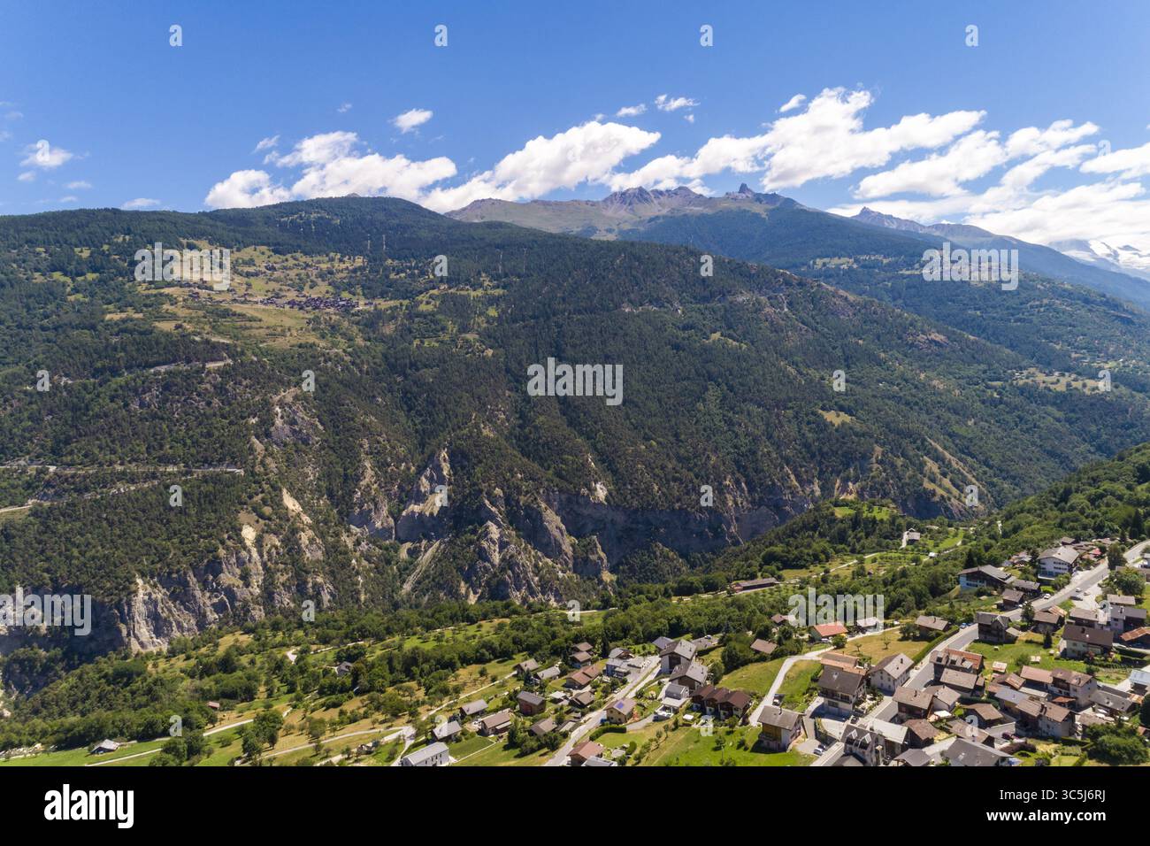 Vista aerea del paesaggio dove il villaggio si trova ai piedi delle maestose montagne, che si fondono completamente con l'arazzo naturale, Vallese, Switz Foto Stock