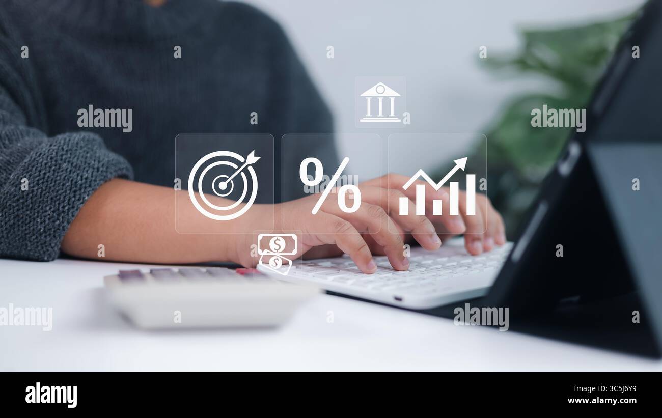 Le icone finanziarie come un target, una percentuale e un grafico di crescita vengono visualizzate in modo olografico quando una persona digita su una tastiera bianca, simboleggiando l'analisi, inv Foto Stock