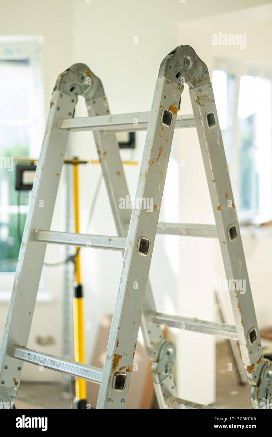 La scala in metallo si trova in una stanza ben illuminata, evidenziandone la struttura e l'usura, circondata da strumenti e materiali di ristrutturazione, creando un'atmosfera fai da te Foto Stock