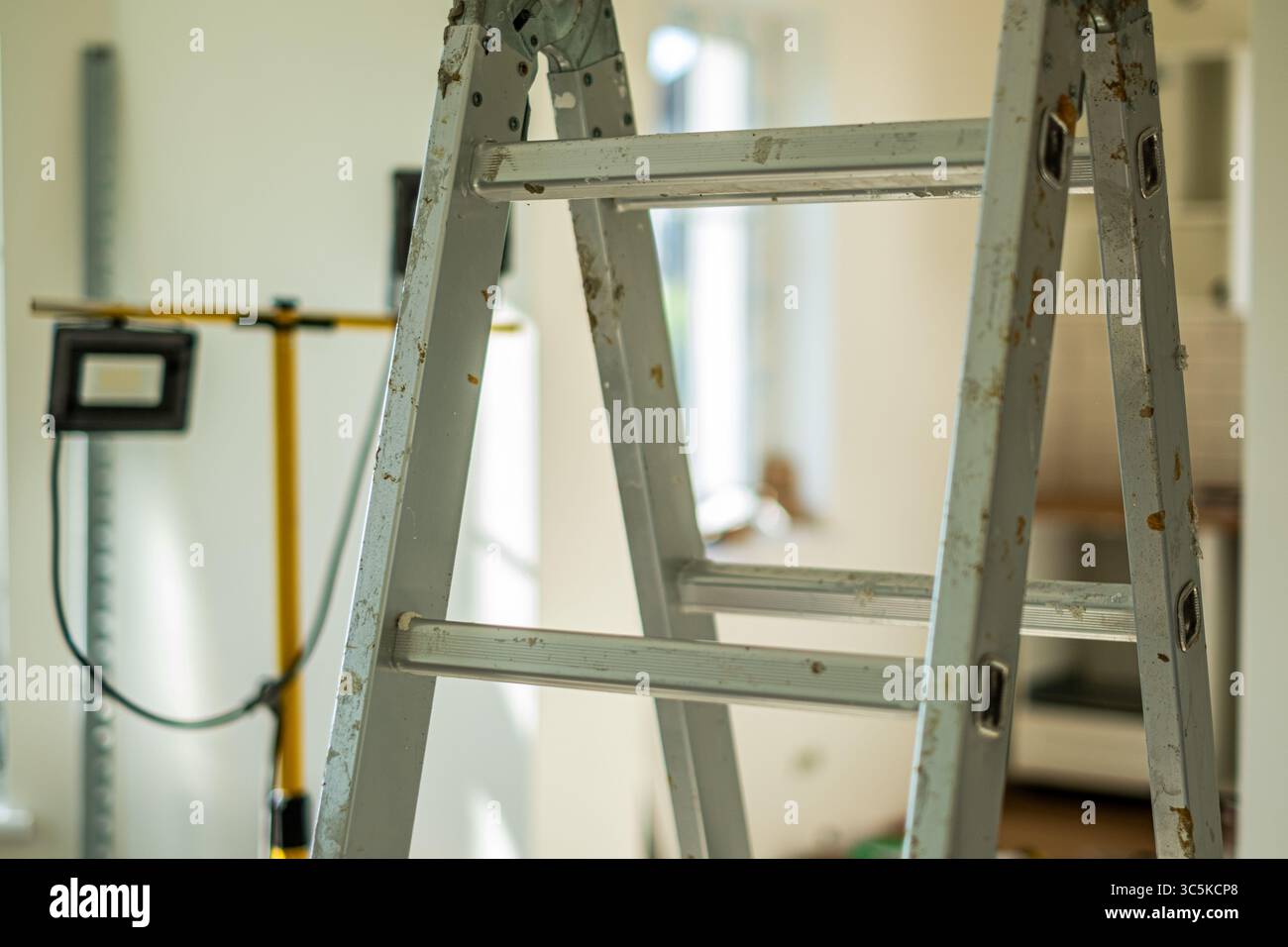 La scala in metallo si trova in una stanza ben illuminata, circondata da strumenti e materiali, creando un'atmosfera di ristrutturazione domestica e lavori di costruzione Foto Stock