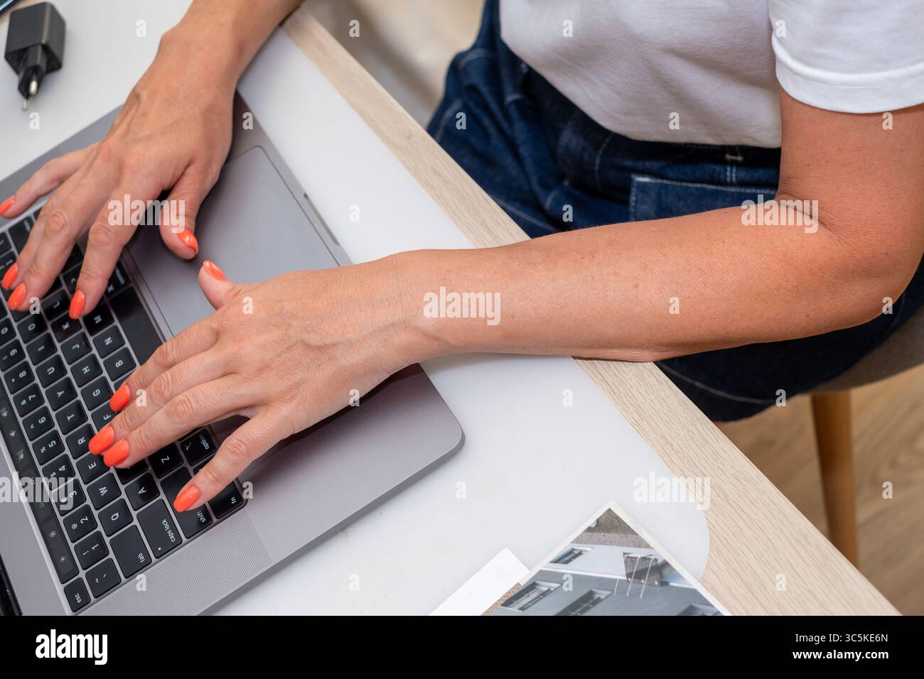 Le mani di una donna con uno smalto brillante sono impegnate nella digitazione su un laptop in uno spazio di lavoro contemporaneo, sottolineando un'atmosfera pulita e organizzata Foto Stock