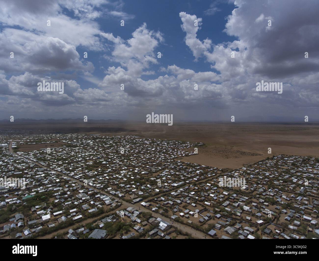 Vista aerea di un fitto insediamento giustapposto al paesaggio arido sotto un vasto cielo, le strutture della città creano un arazzo testurizzato contro i toni della terra, Kakuma, Turkana County, Kenya. Foto Stock