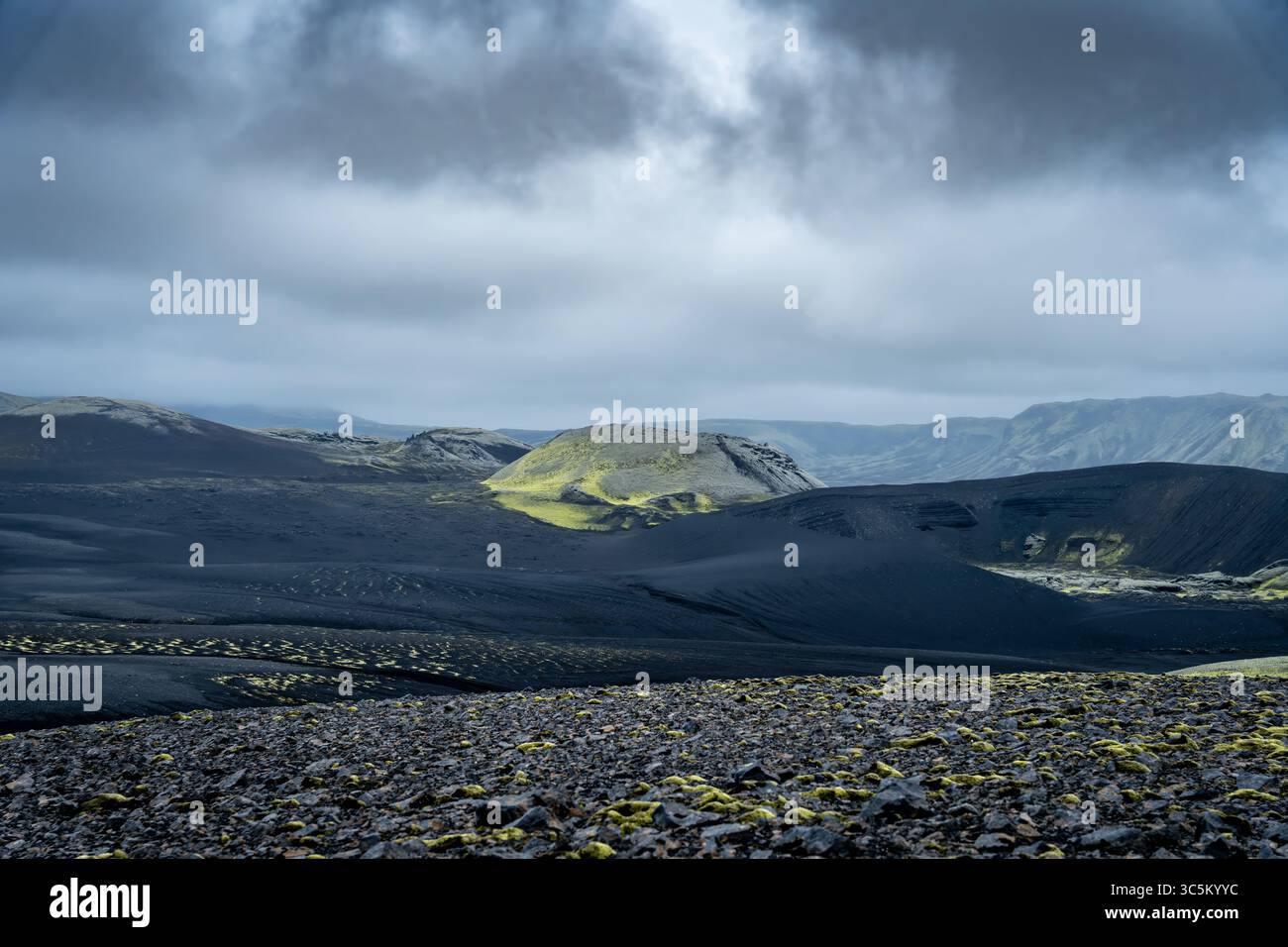 Vista delle colline verdi e umide che contrastano con l'aspro e scuro paesaggio vulcanico sotto un cielo nuvoloso, Kirkjubaejarklaustur, Skaftárhreppur, Islanda. Foto Stock