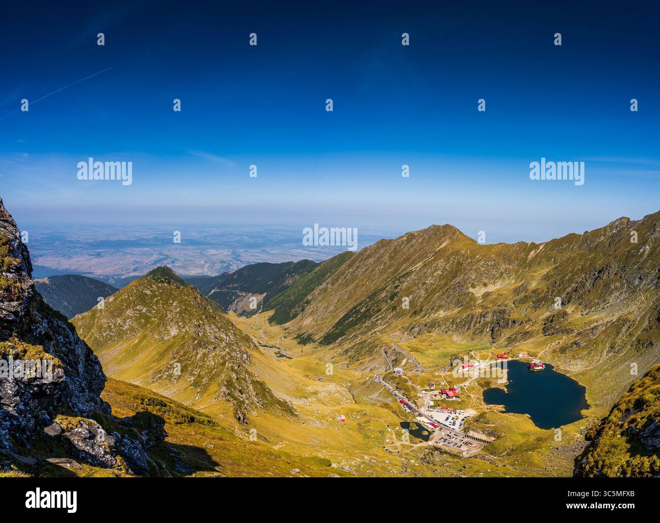 Un paesaggio alpino dei Monti Fagaras in Romania, con il tranquillo lago Balea circondato da colline rocciose. Il giorno estivo è luminoso e soleggiato, Foto Stock