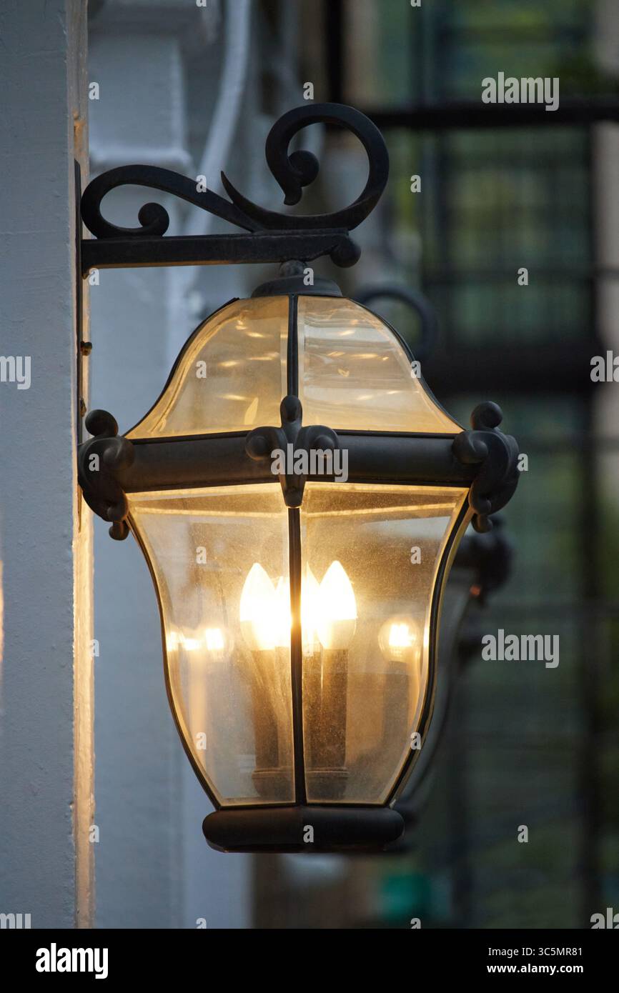 applique in ferro battuto nero in stile vittoriano sulla parete esterna di un condominio, illuminazione decorativa illuminata Foto Stock
