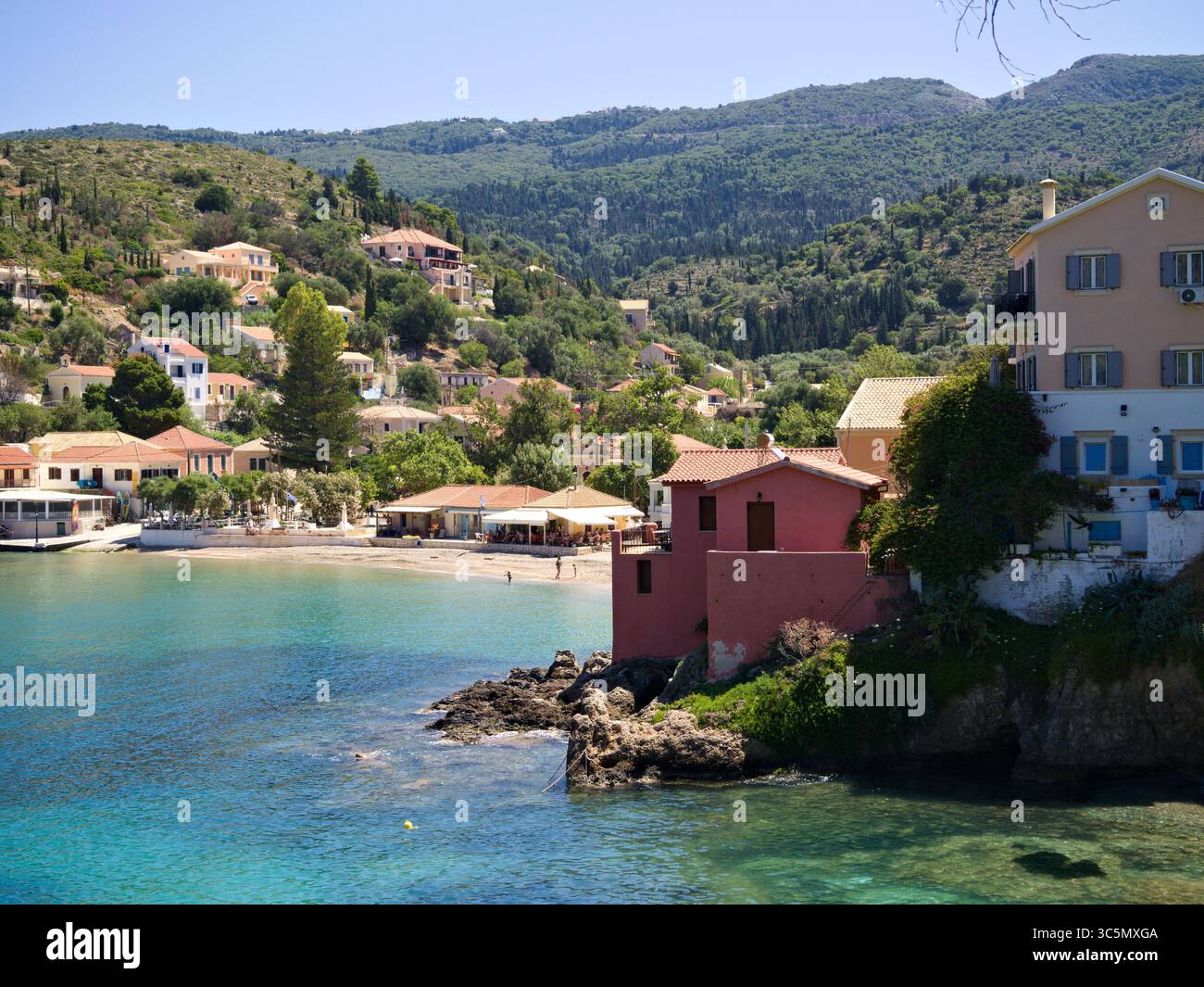 Vista costiera di Assos, Cefalonia, caratterizzata dalla tradizionale architettura greca e lussureggianti colline sul Mar Ionio. Foto Stock