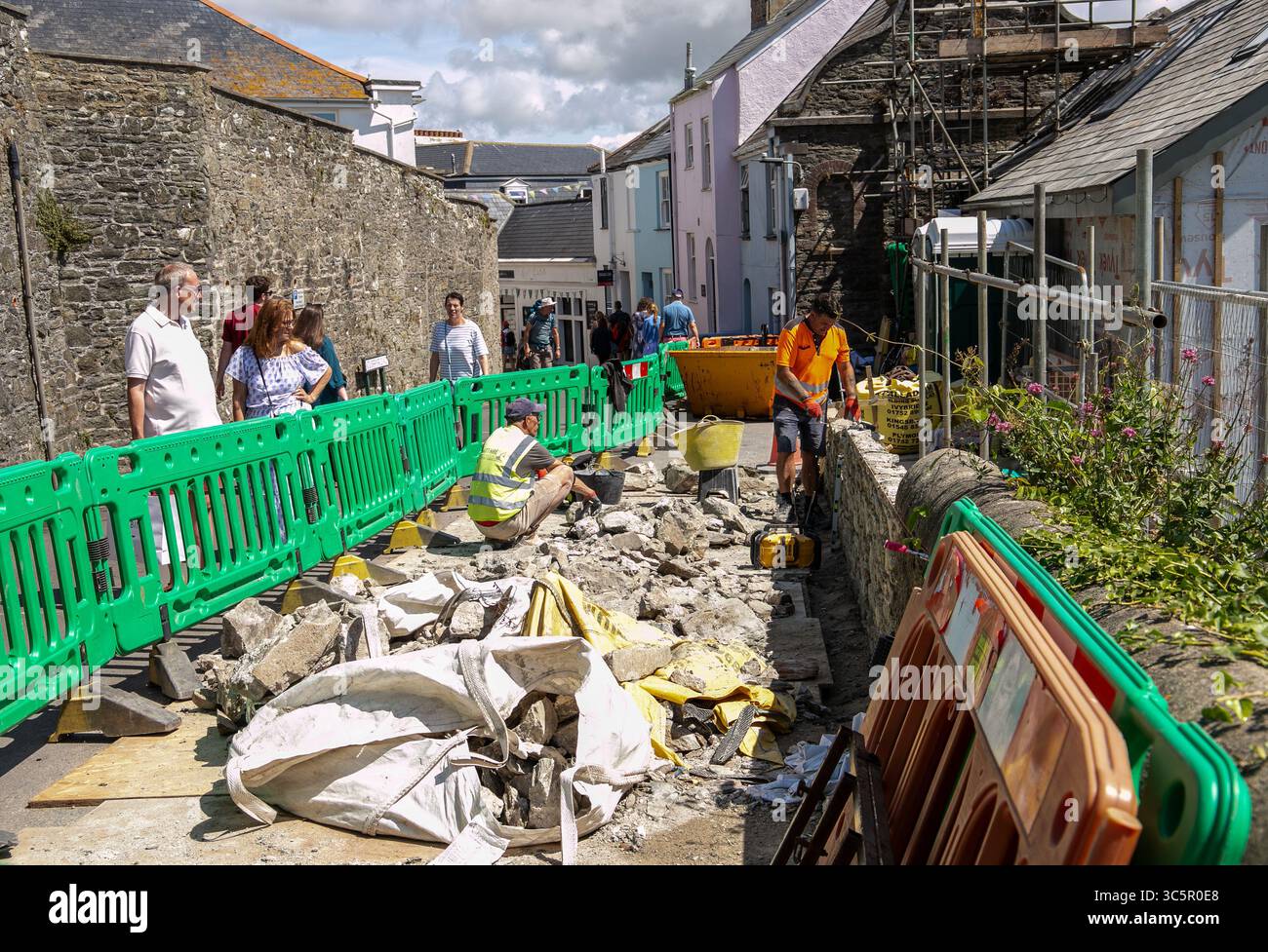Operai edili che ristrutturano una stretta parete stradale in un'area residenziale con osservatori e materiali da costruzione sparsi intorno a Salcombe Devon Foto Stock