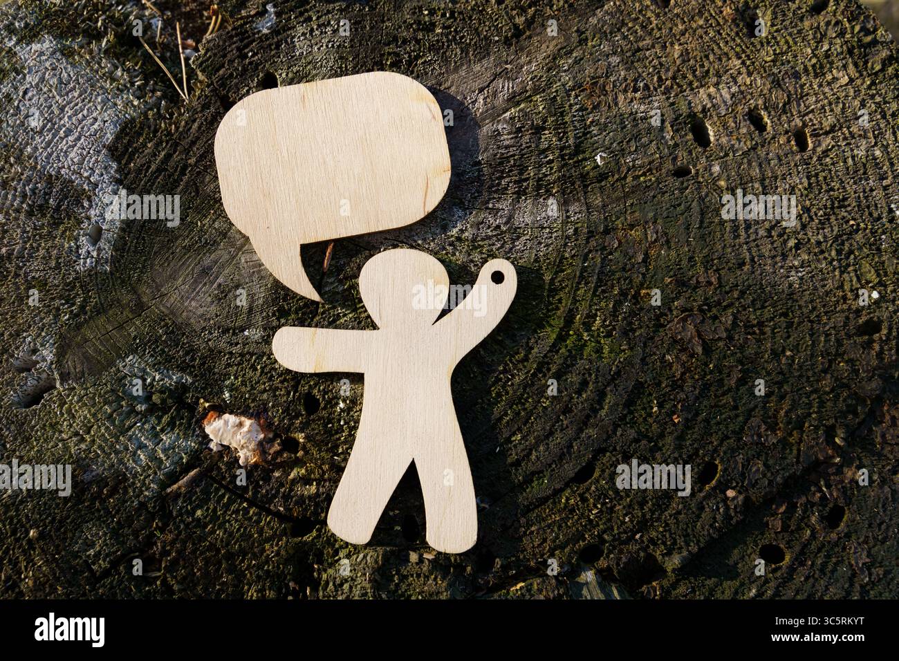 Una figura di legno si erge su un ceppo d'albero rustico, braccia sollevate come se condividesse i pensieri. Sopra di essa, una bolla di discorso suggerisce comunicazione e creatività ami Foto Stock