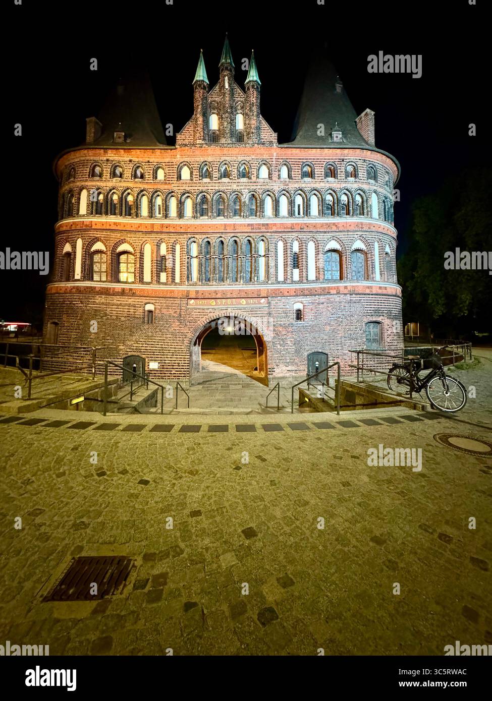 L'iconico Holstentor di Lubecca, Germania, splendidamente illuminato di notte, che mostra l'architettura medievale della storica porta della città. - Immagine stock catturata con smartphone