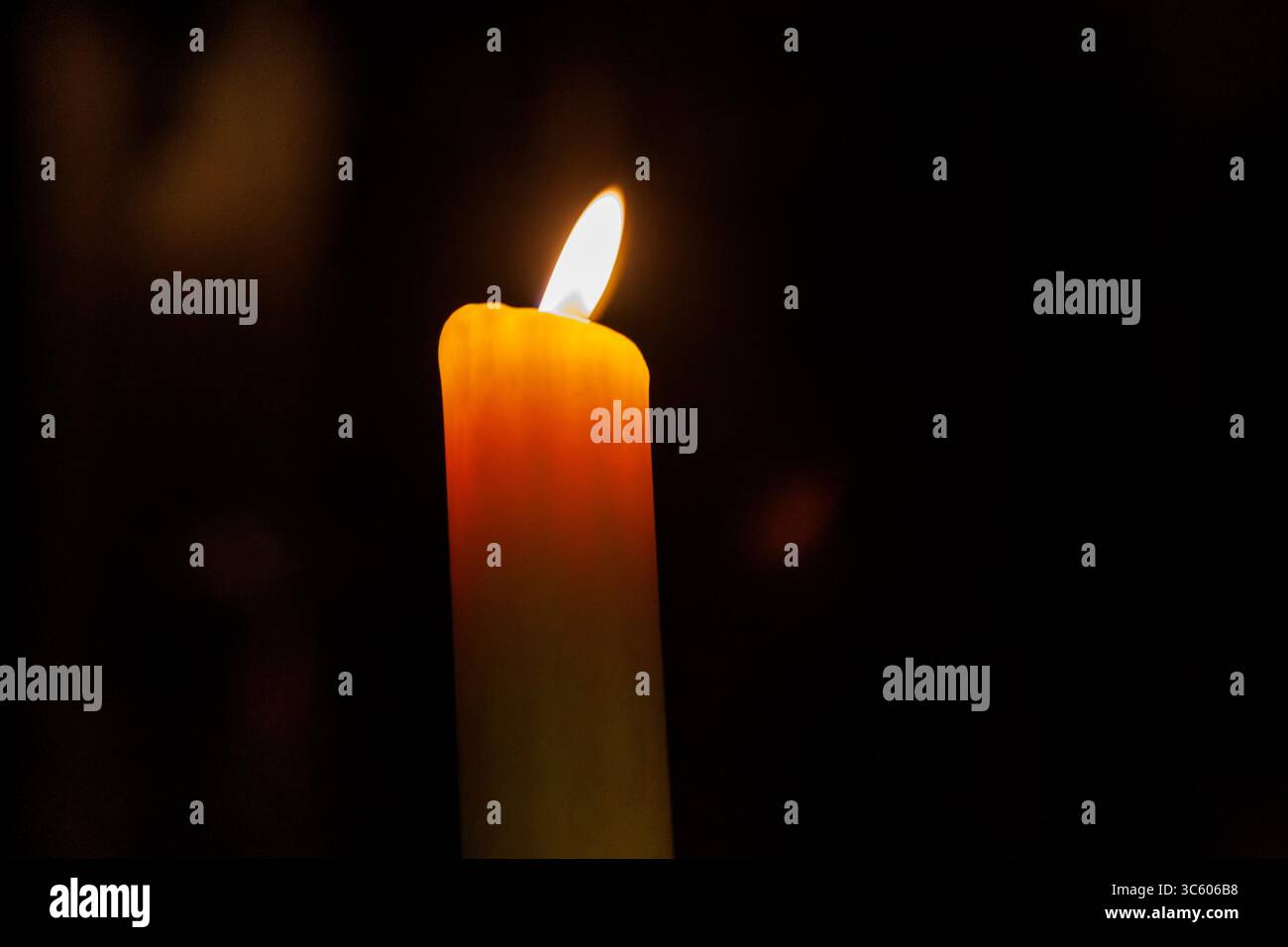 Una singola candela è alta e la sua fiamma tremola con la luce calda che emette una luce soffusa Foto Stock