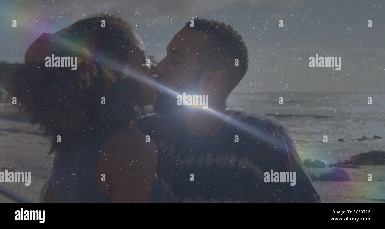 Coppia che si baciano indossando un abbigliamento casual sul vialetto della spiaggia con ringhiere in metallo, spiaggia sabbiosa e onde dell'oceano Foto Stock