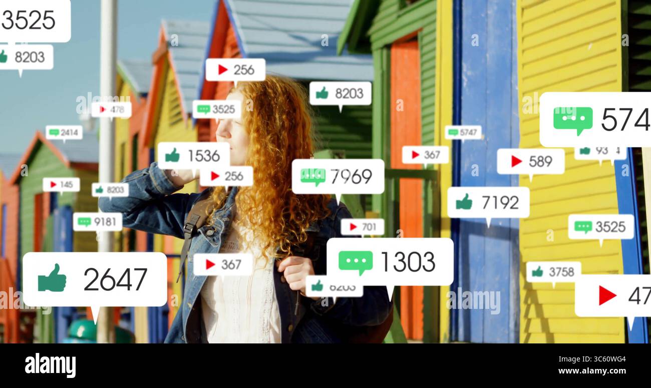 Una donna rossa che indossa una giacca in denim sullo smartphone in baite sulla spiaggia con notifiche fluttuanti Foto Stock