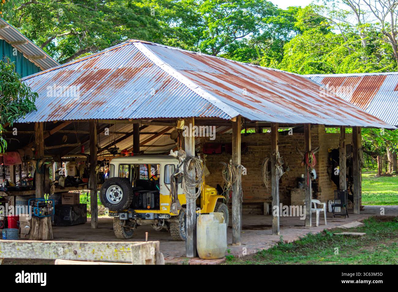 Un vivace capannone agricolo caratterizzato da architettura rustica e veicoli, circondato da lussureggiante vegetazione a Casanare, Colombia. Ideale per immagini a tema naturale. Foto Stock