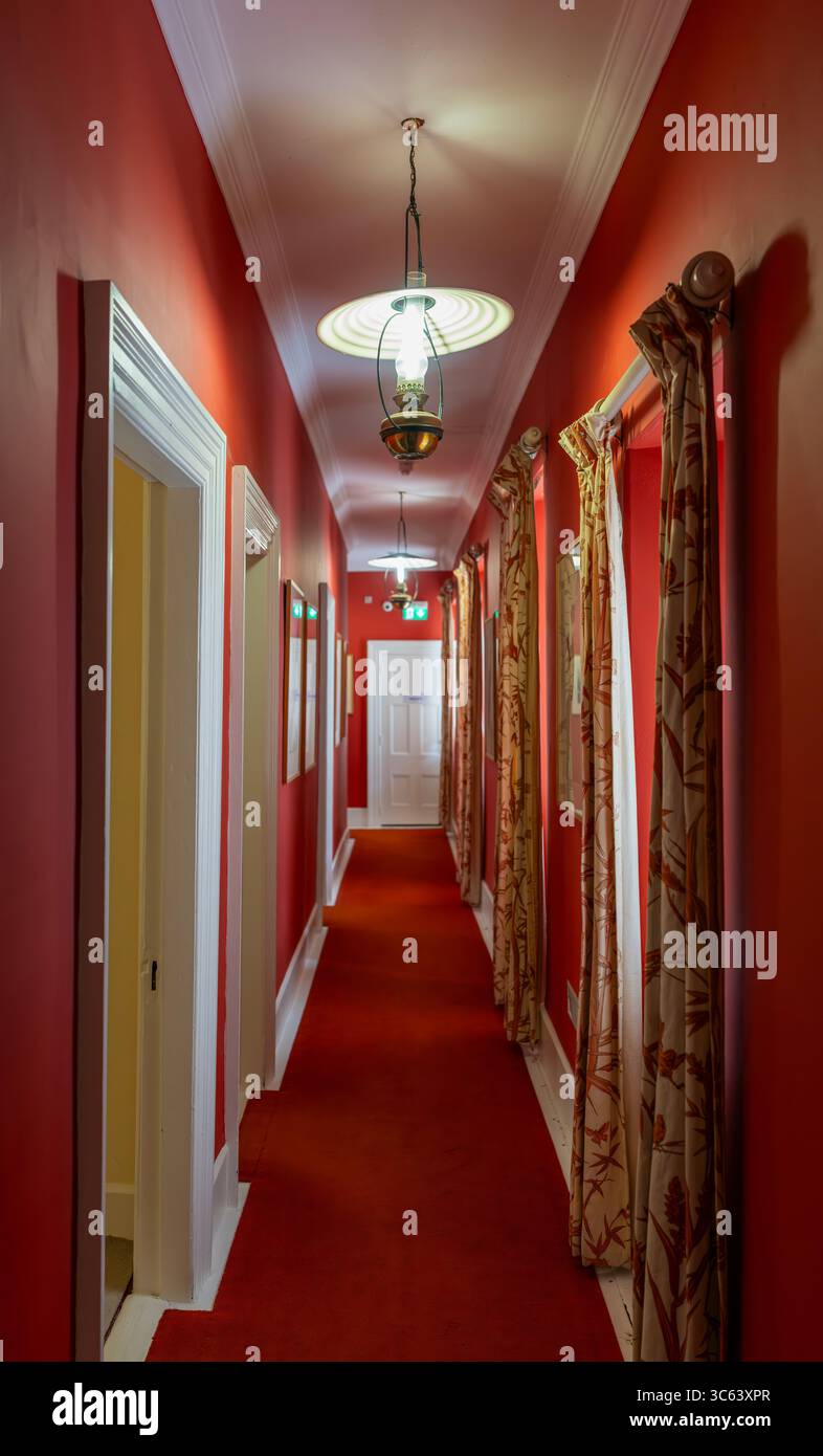 Corridoio rosso interno del castello di Glenveagh nel Glenveagh National Park, contea di Donegal, Irlanda, con lampade a sospensione, tappeto rosso, e tende a motivi geometrici. Foto Stock